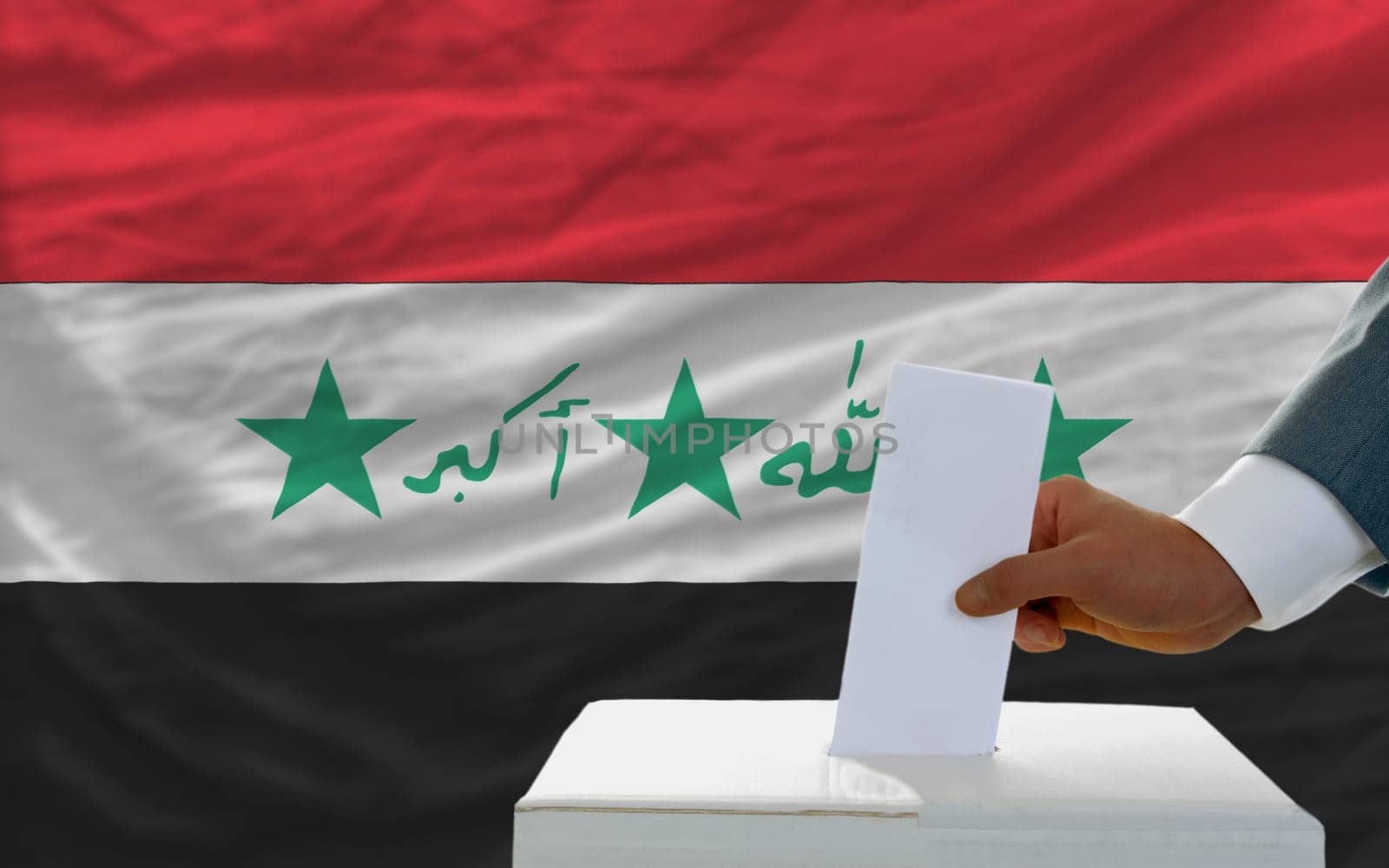man putting ballot in a box during elections in iraq in fornt of flag