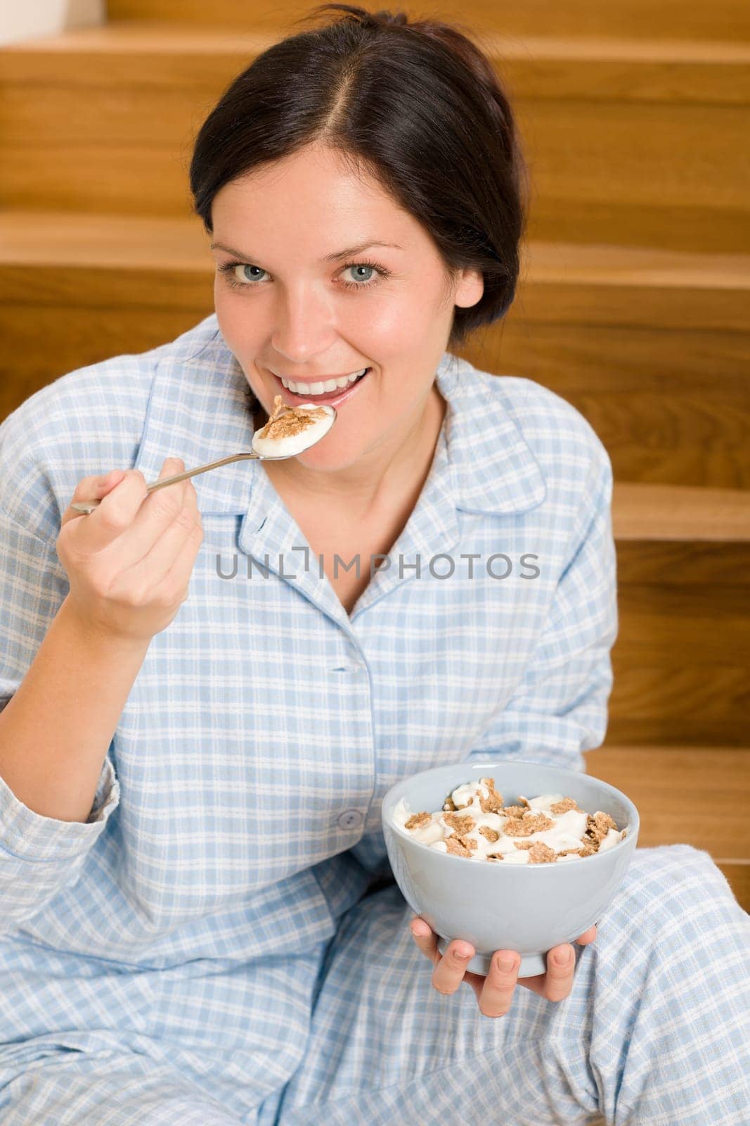 Home breakfast happy woman in pajamas eating cereals on stairs
