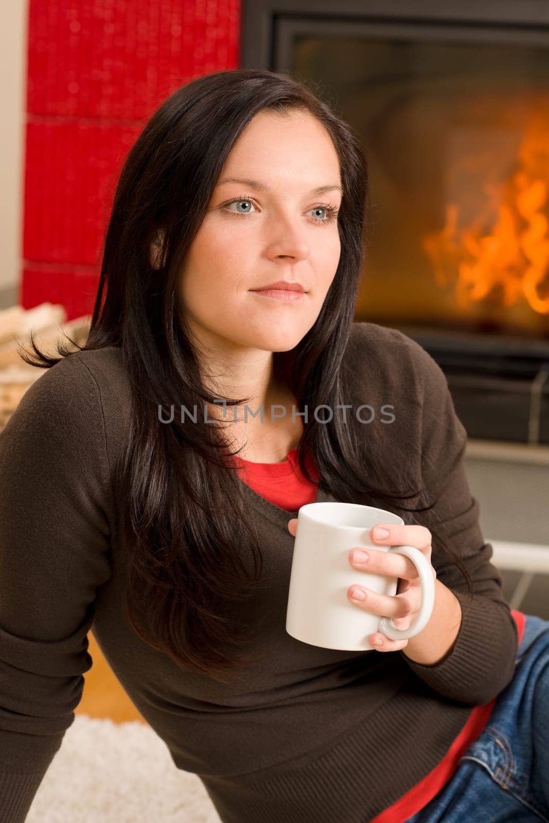 Young woman enjoying winter hot drink by home fireplace