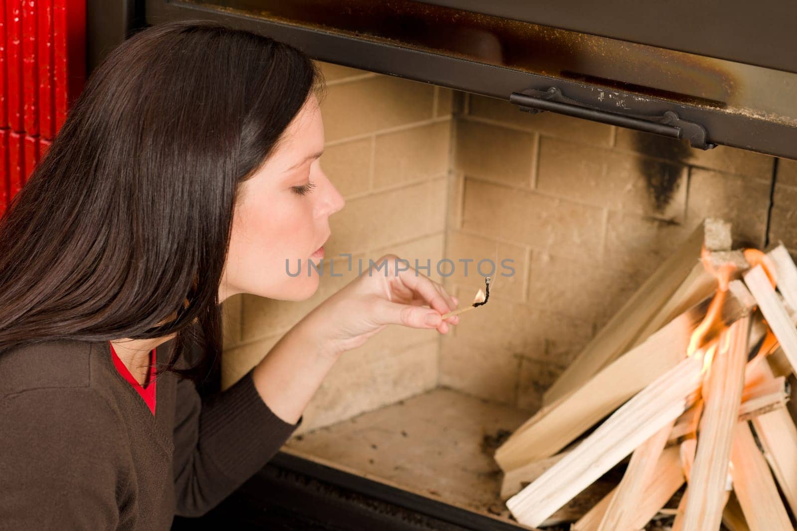 Young woman lighting up wood logs in fireplace home living
