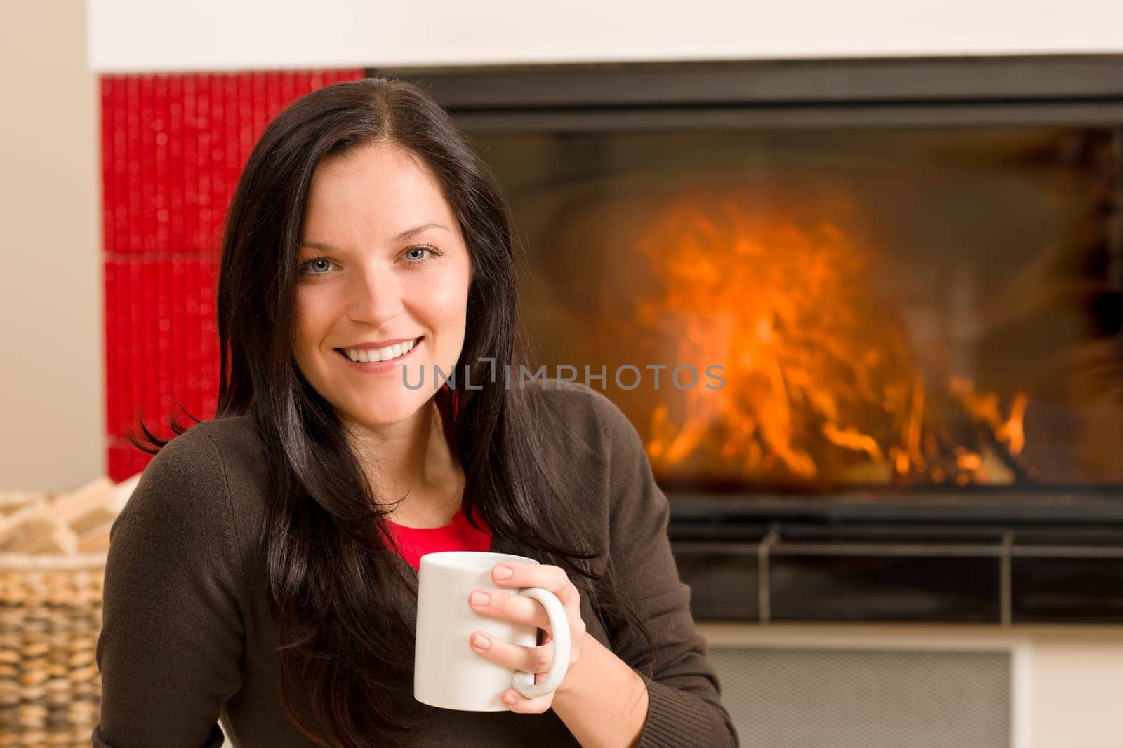 Young woman enjoying winter hot drink by home fireplace