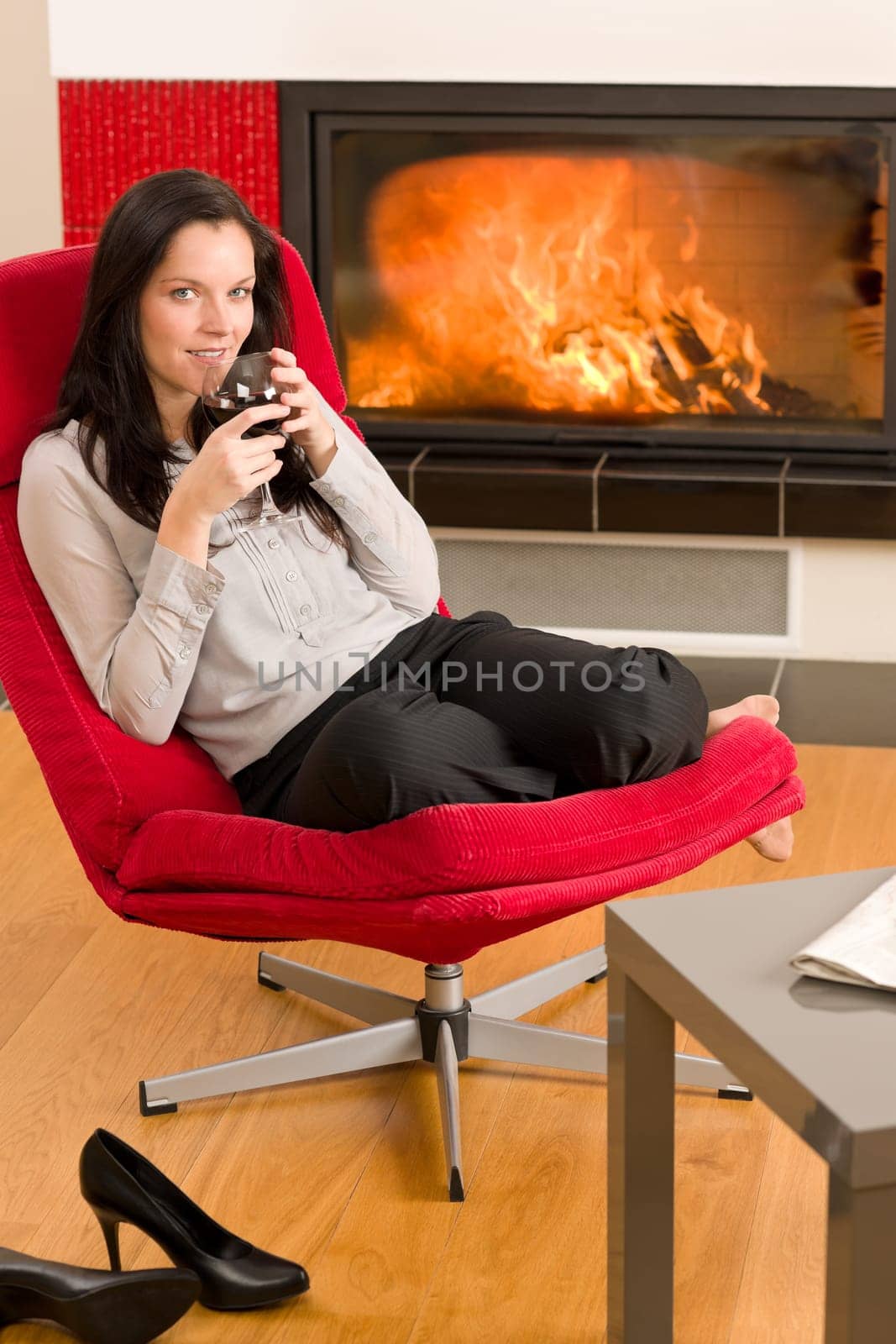 Young woman enjoying glass of red wine by home fireplace