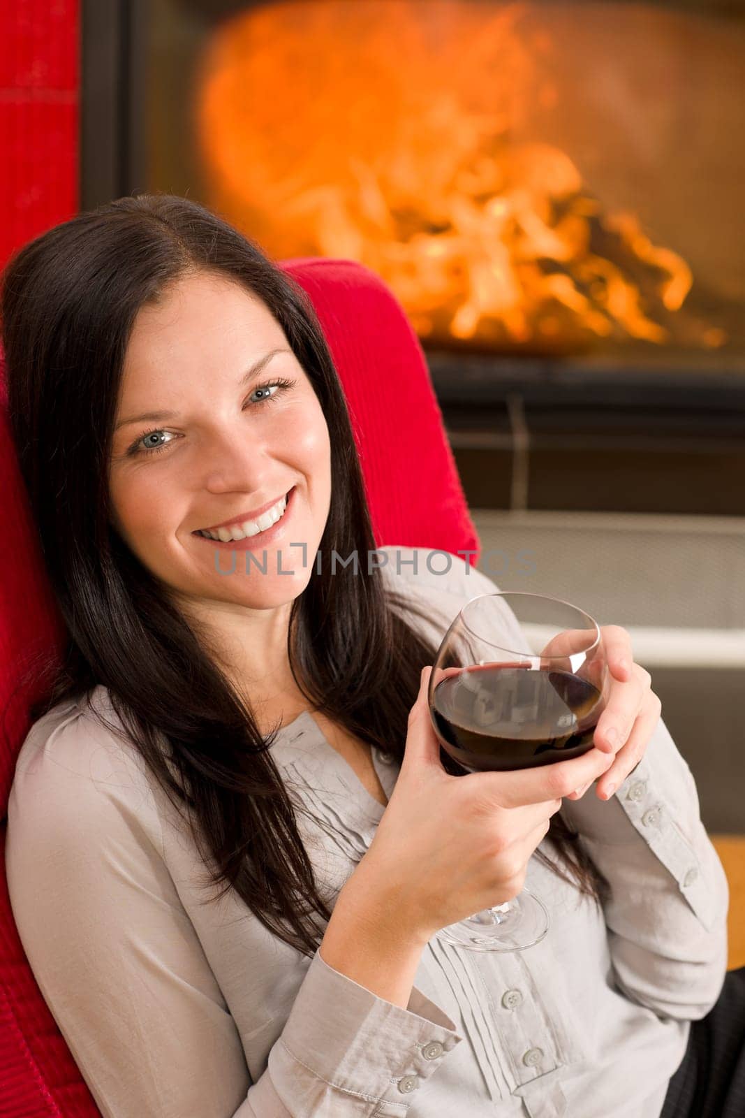 Young woman enjoying glass of red wine by home fireplace