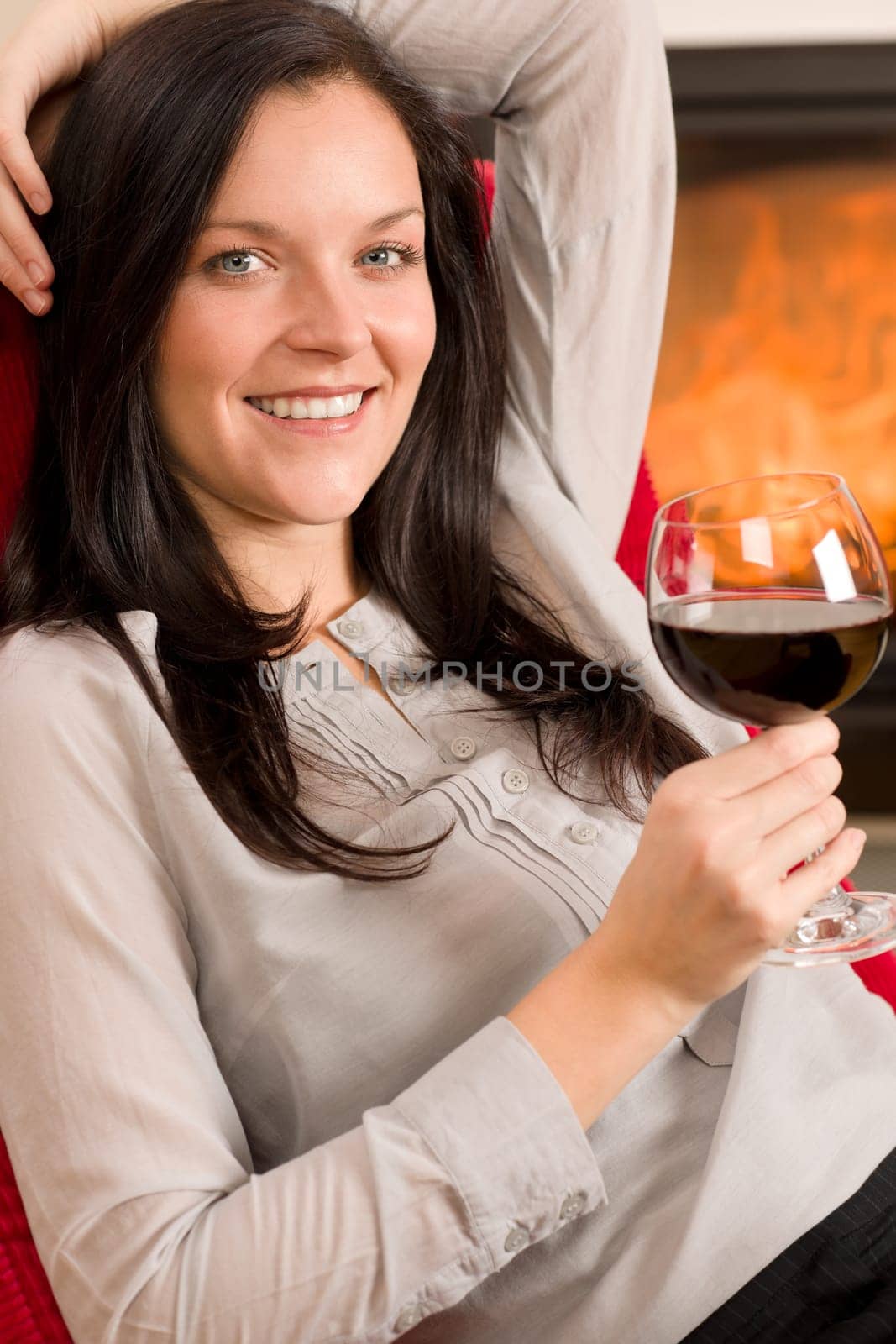 Young woman enjoying glass of red wine by home fireplace