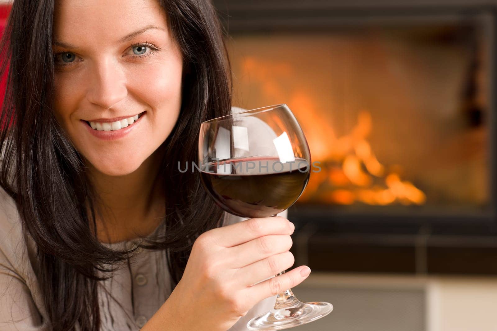 Young woman enjoying glass of red wine by home fireplace