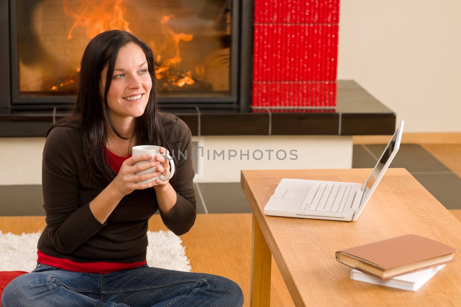 Happy woman at fireplace with laptop enjoying winter hot drink