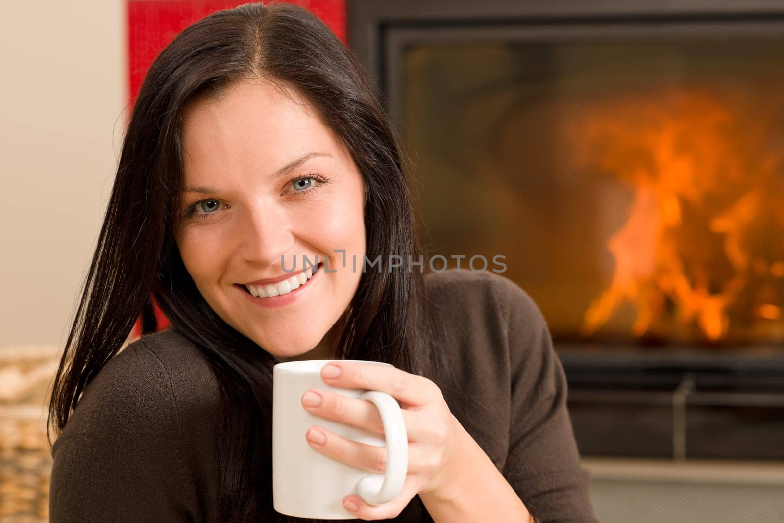 Young woman enjoying winter hot drink by home fireplace