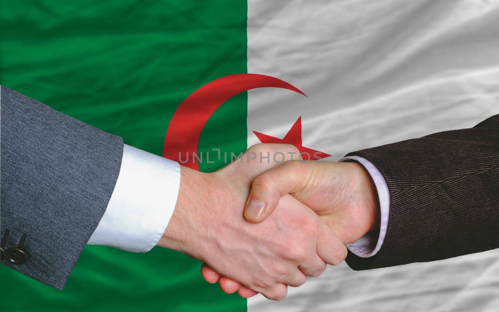 two businessmen shaking hands after good business investment  agreement in algeria, in front of flag