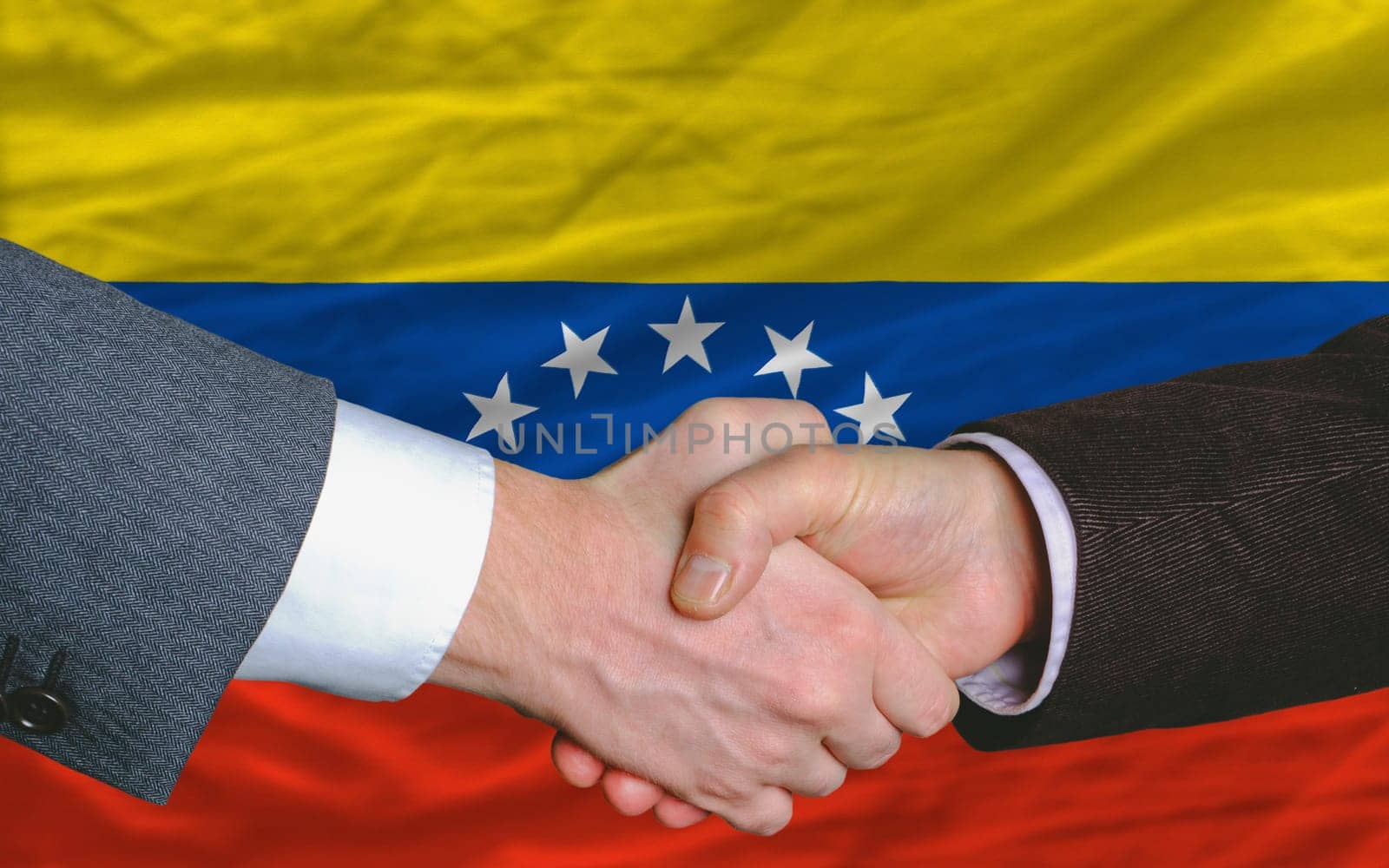 two businessmen shaking hands after good business investment  agreement in venezuela, in front of flag