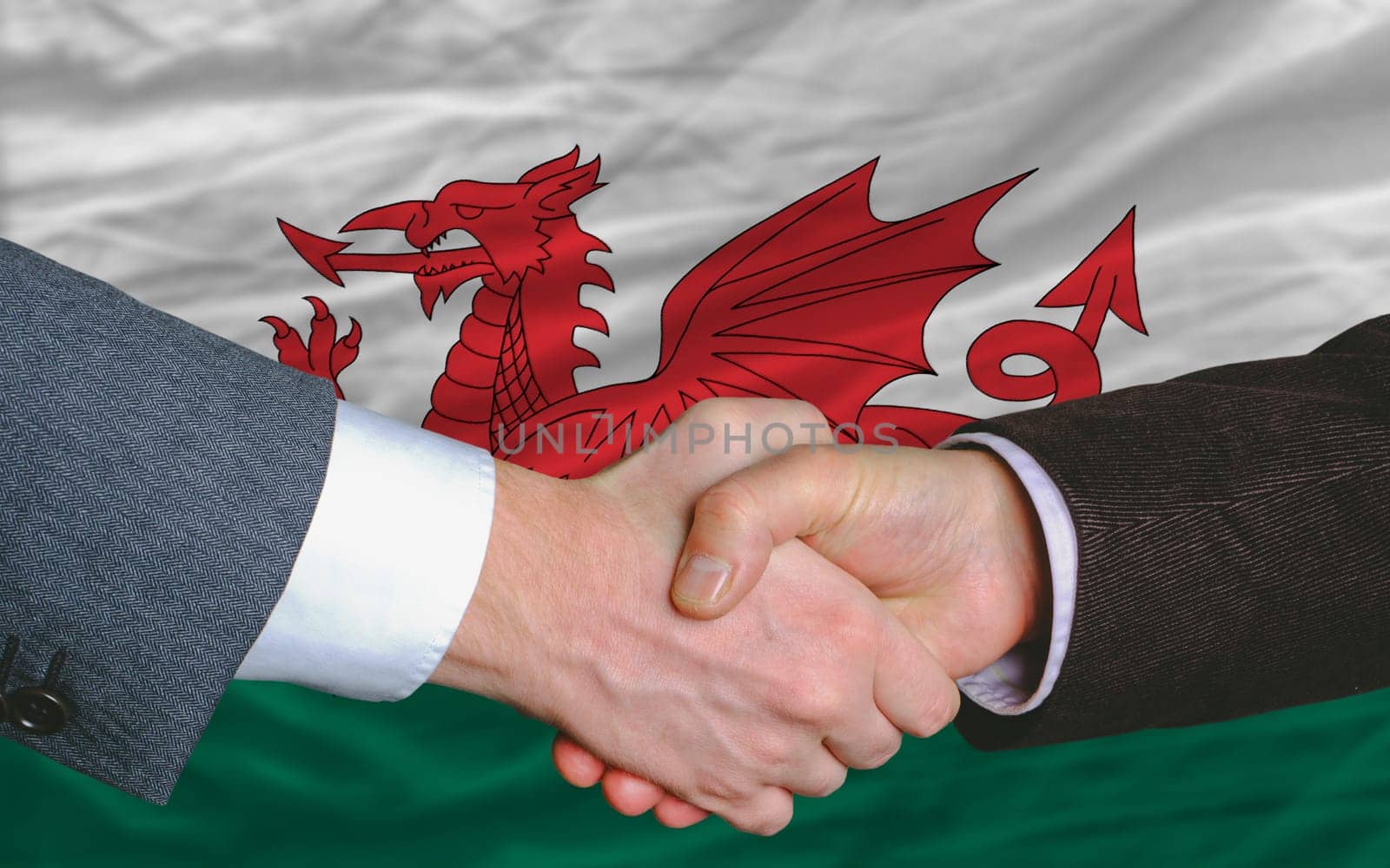 two businessmen shaking hands after good business investment  agreement in wales, in front of flag