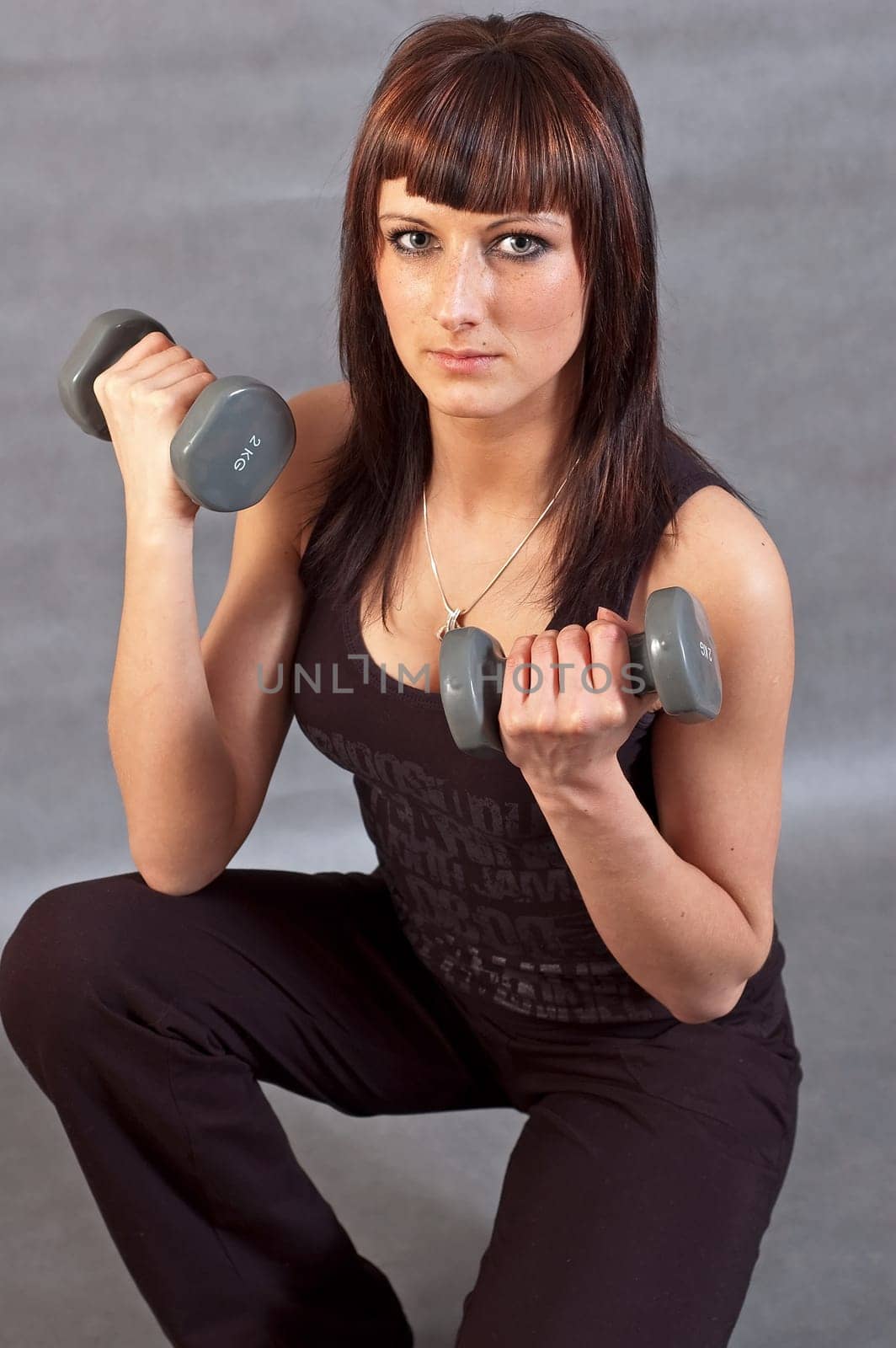 young woman lifting weights on gray background
