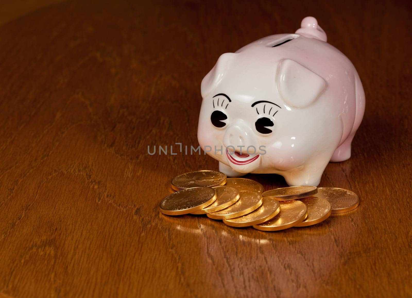 Pink piggybank on a wooden table with pile of gold eagle coins