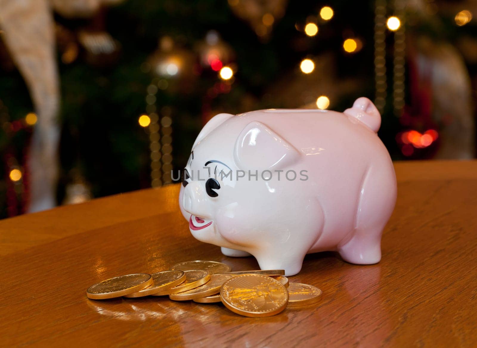 Pink piggybank on a wooden table in front of a christmas tree with gold coins