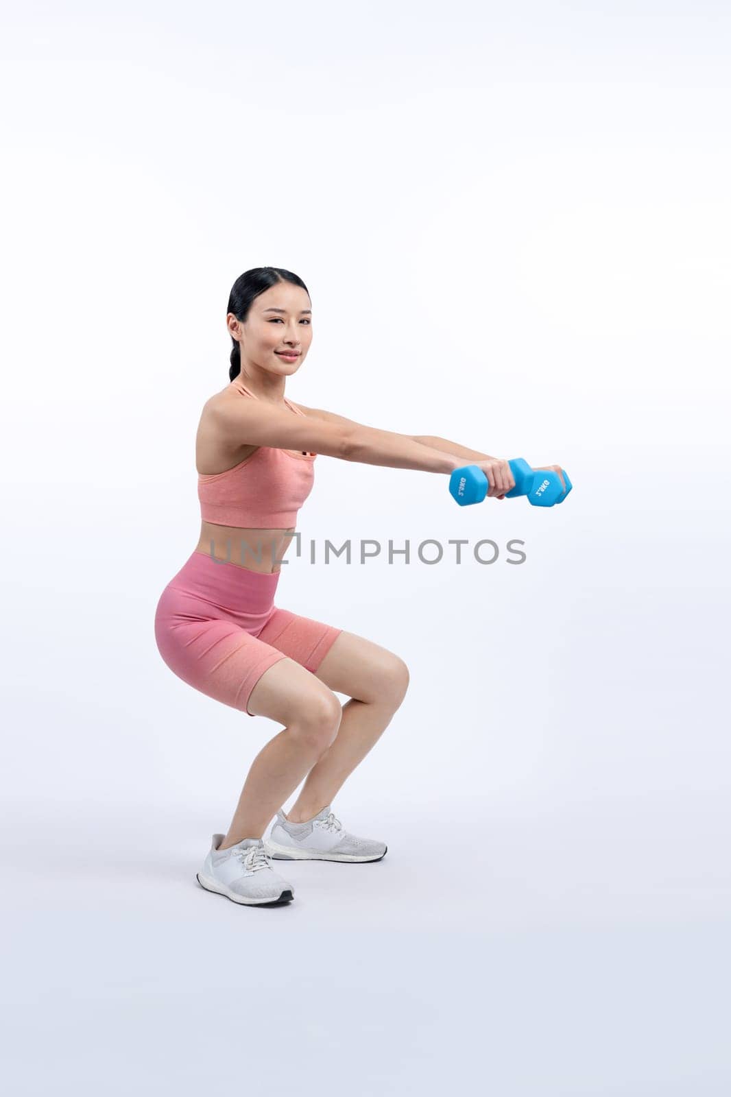 Vigorous energetic woman doing dumbbell weight lifting exercise on isolated background. Young athletic asian woman strength and endurance training session as body workout routine.