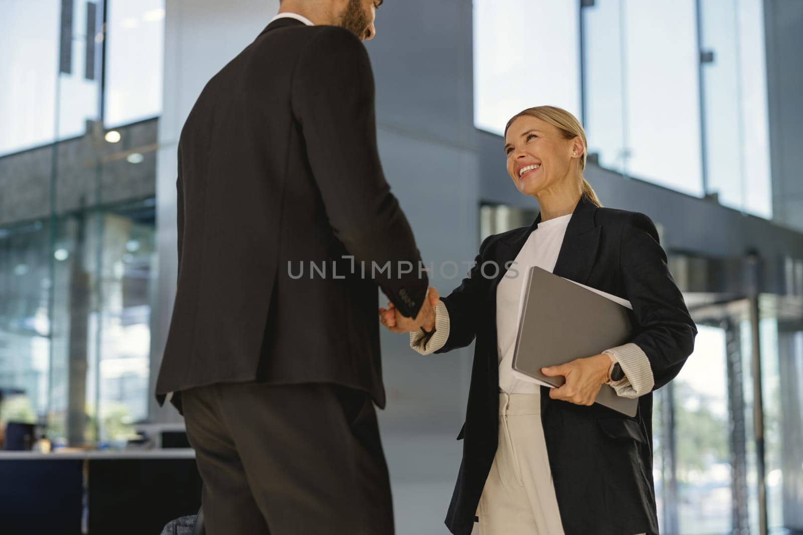 Business partners shaking hands in front of the modern building background. High quality photo
