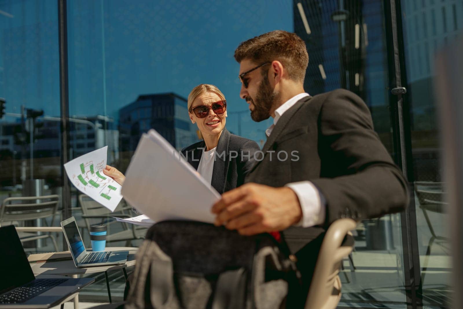 Two business partners working with documents sitting outside of office on cafe terrace by Yaroslav_astakhov