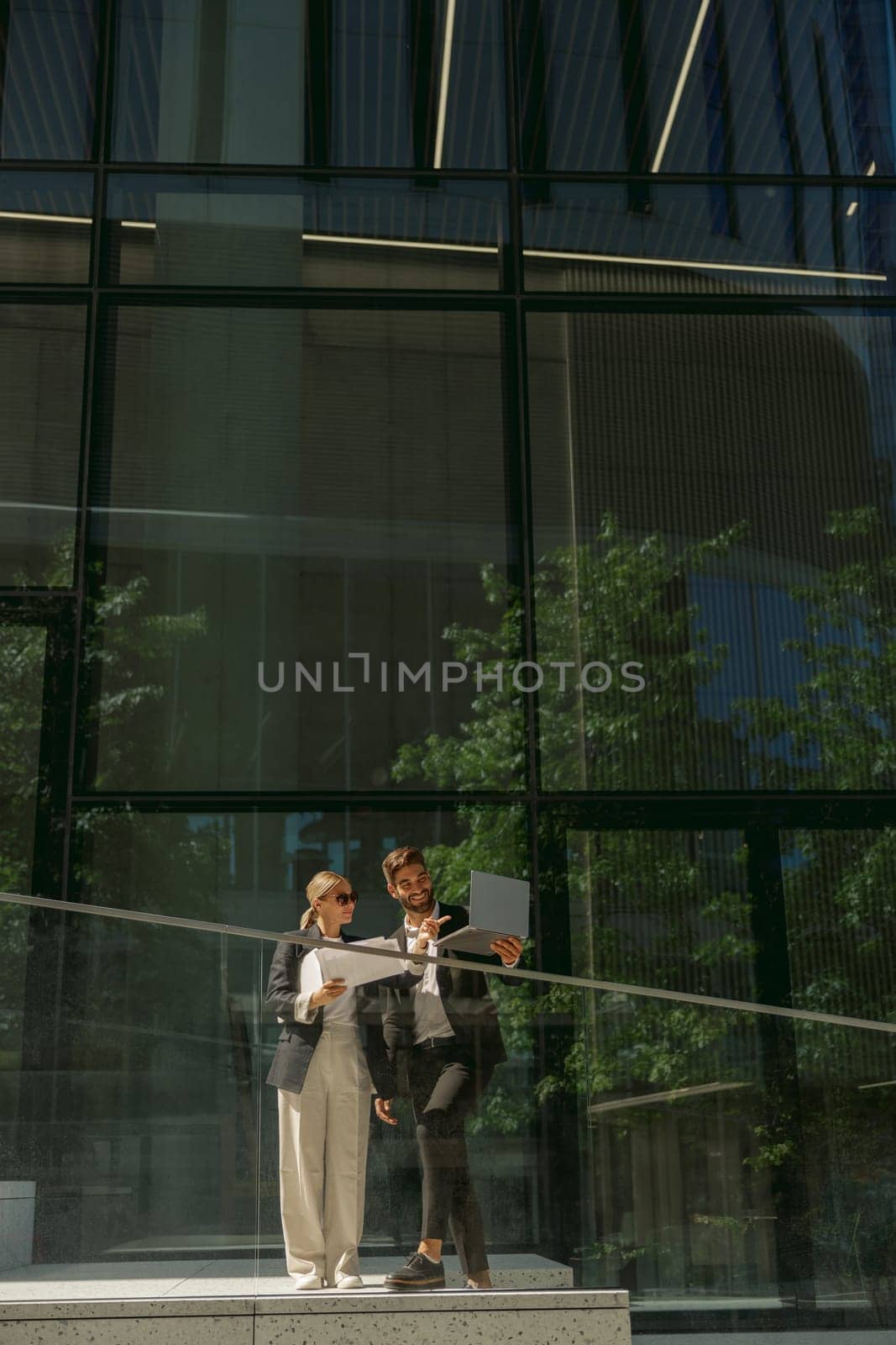 Business colleagues working with documents while standing on background of modern office building by Yaroslav_astakhov