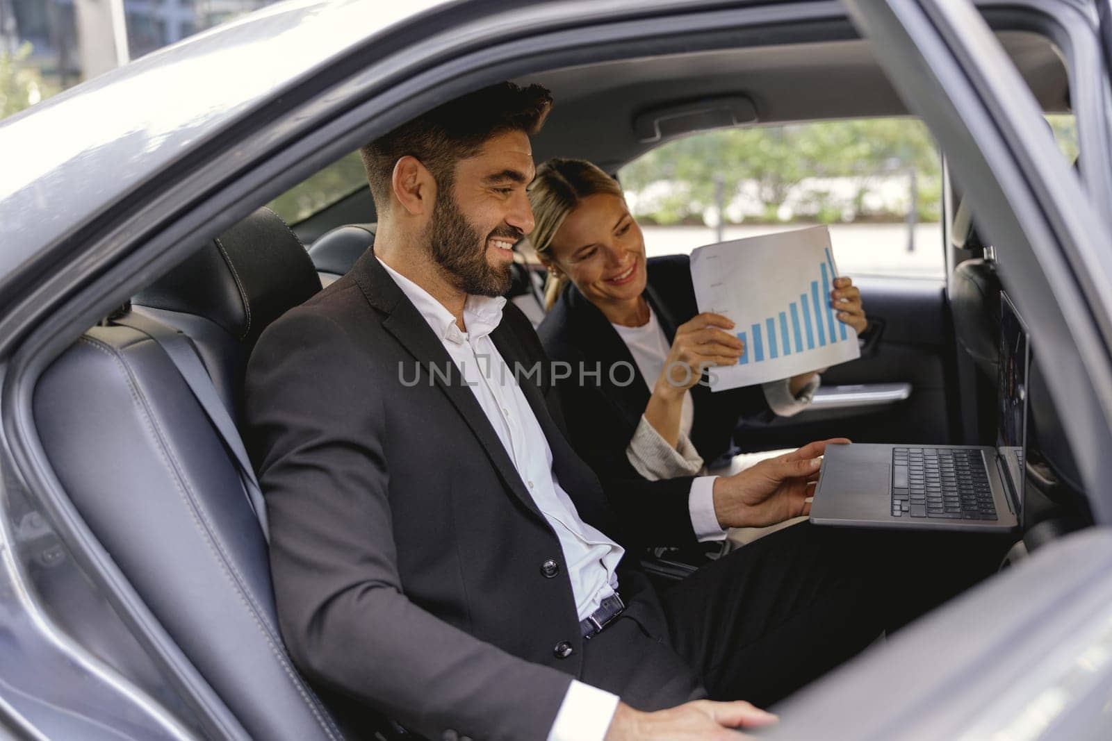 Smiling business analysts have online meeting using laptop while sitting in car back seats by Yaroslav_astakhov