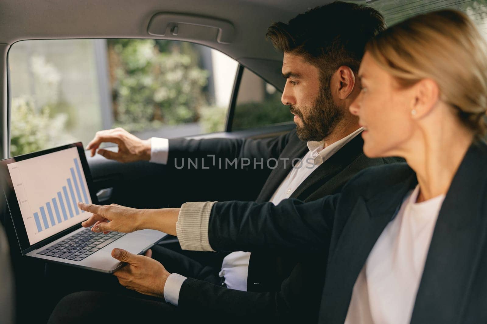 Business colleagues working on laptop in back seat of car while traveling to meeting