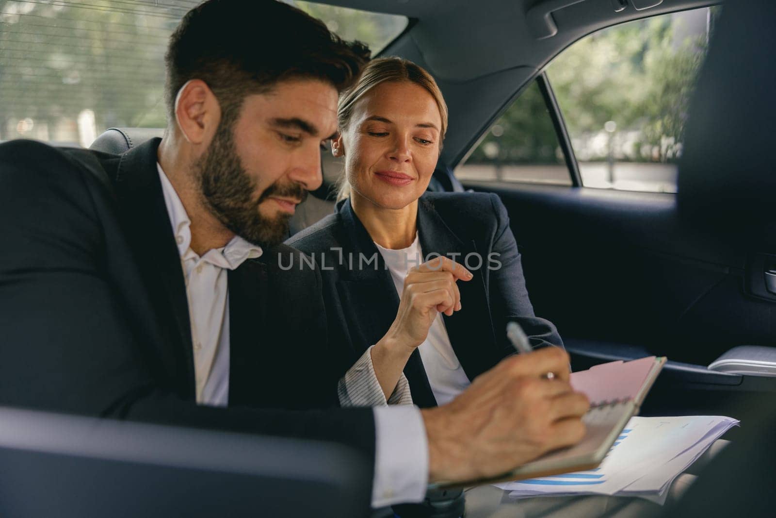 Business colleagues working on document in back seat of car while traveling to meeting
