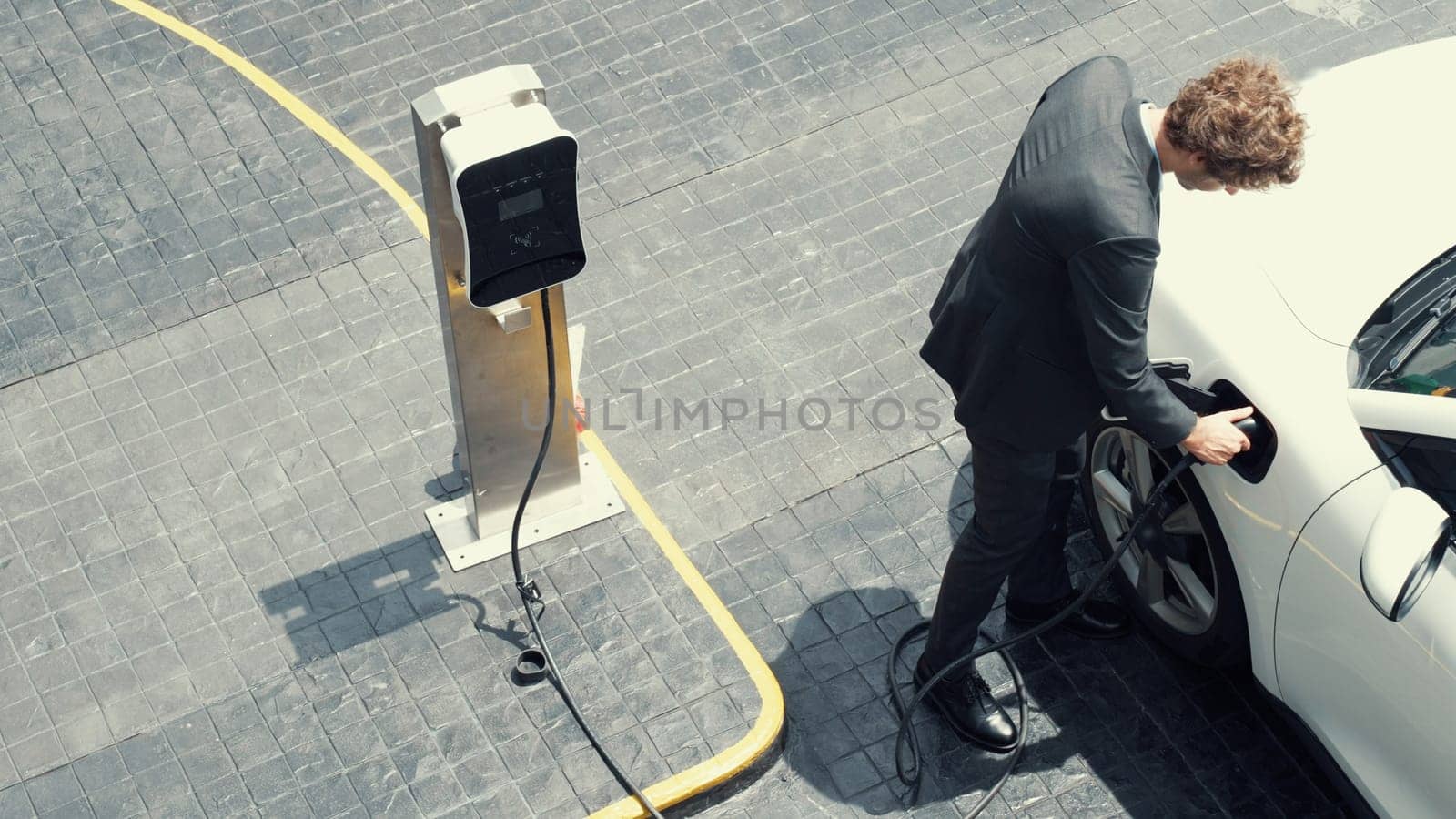 Progressive businessman unplugs charger plug from charging station to his electric car before driving around city center. Eco friendly rechargeable car powered by sustainable and clean energy.