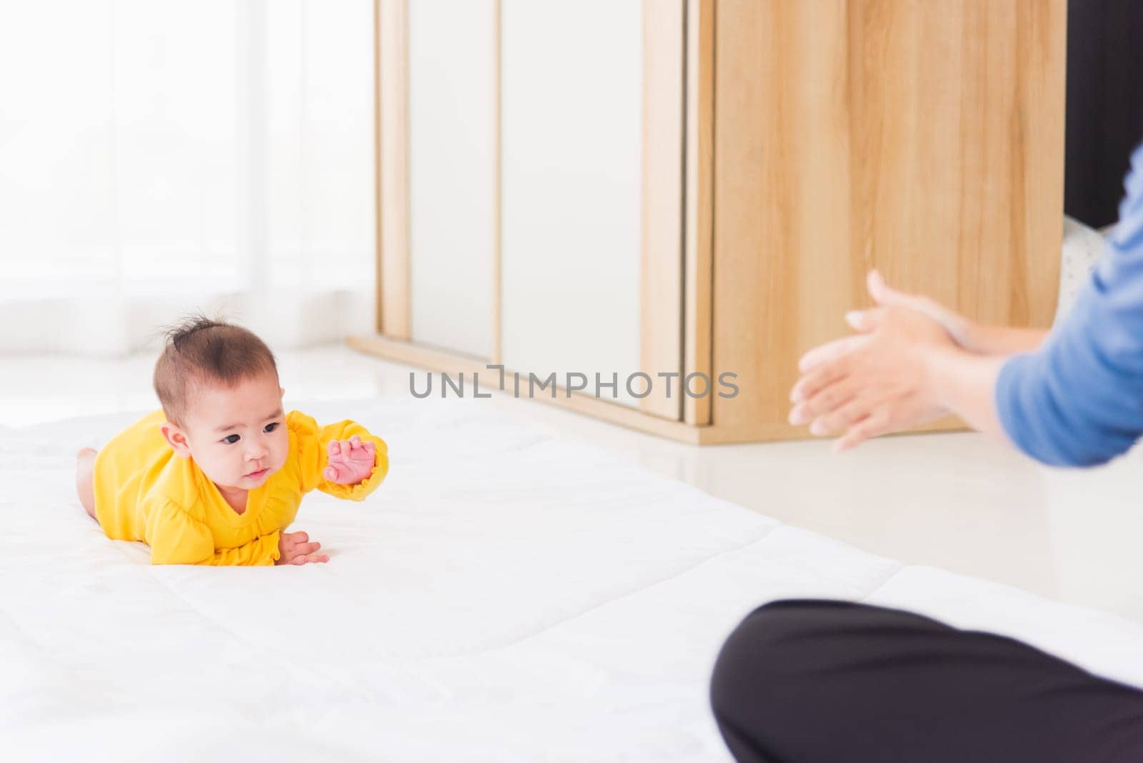 Asian happy young mother have fun learn walking crawling his daughter baby indoors bedroom at home. The mom playing with her little baby to crawl, two family