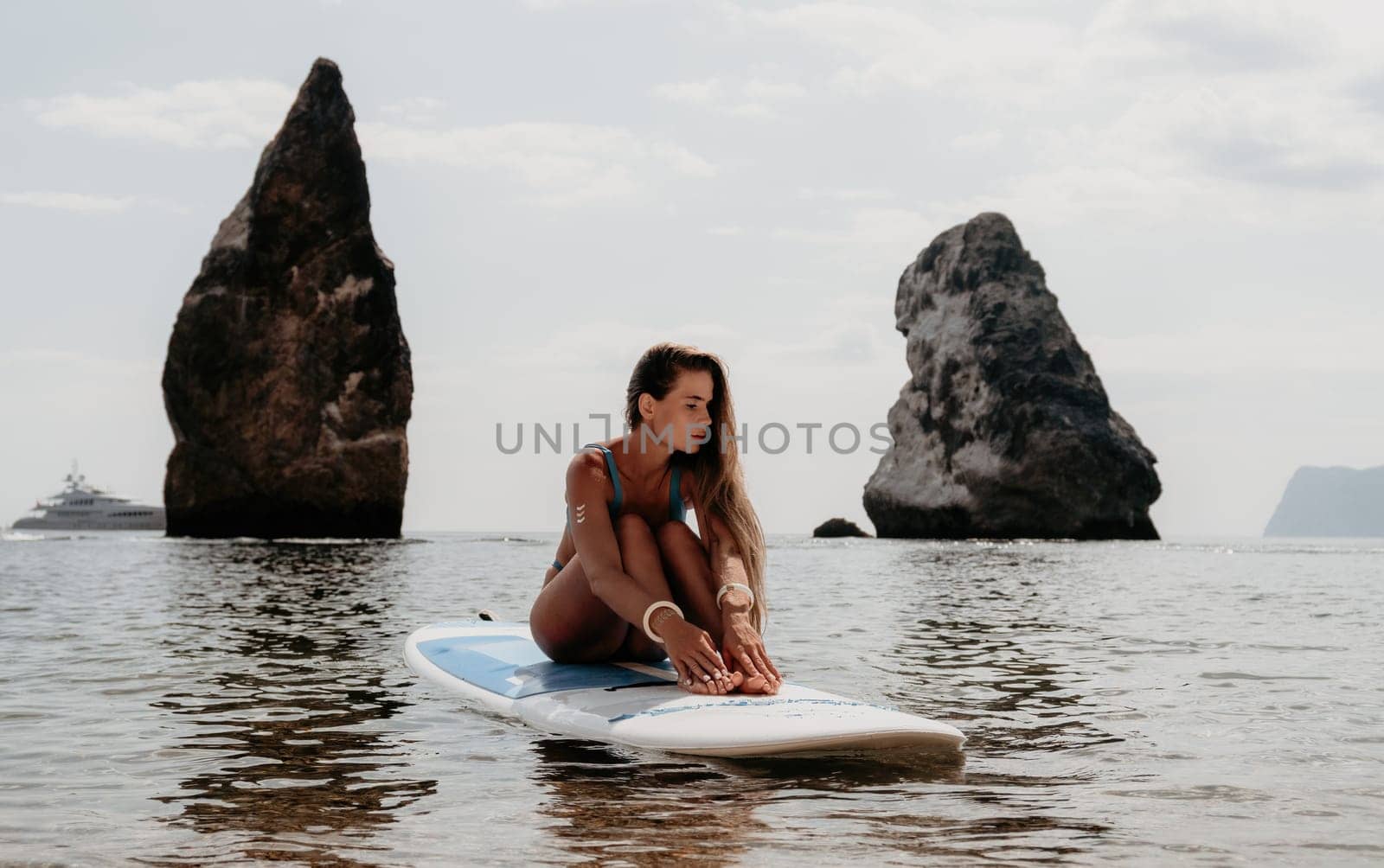 Close up shot of beautiful young caucasian woman with black hair and freckles looking at camera and smiling. Cute woman portrait in a pink bikini posing on a volcanic rock high above the sea