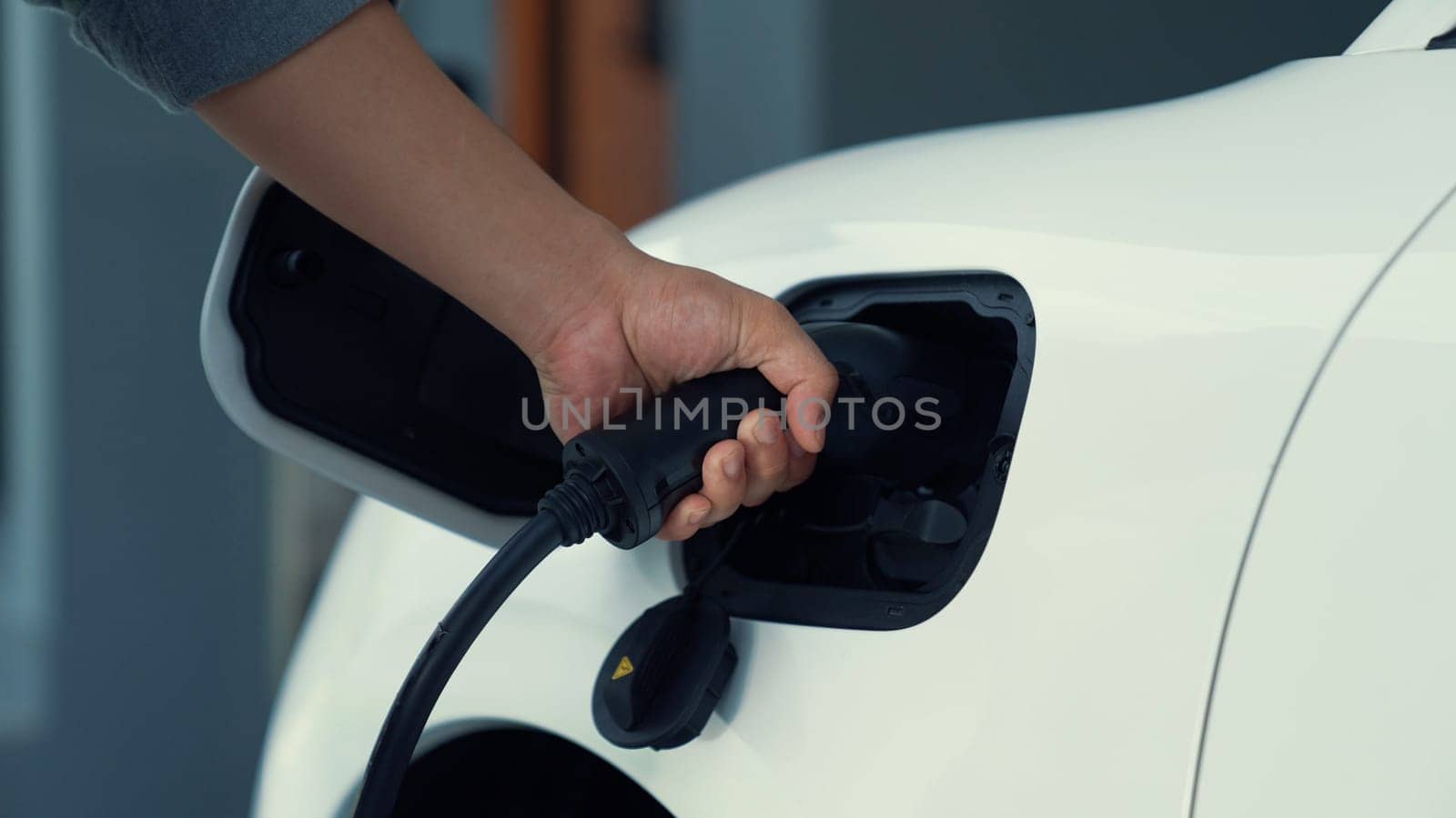 Progressive man attaches an emission-free power connector to the battery of electric vehicle at his home. Electric vehicle charging via cable from charging station to EV car battery