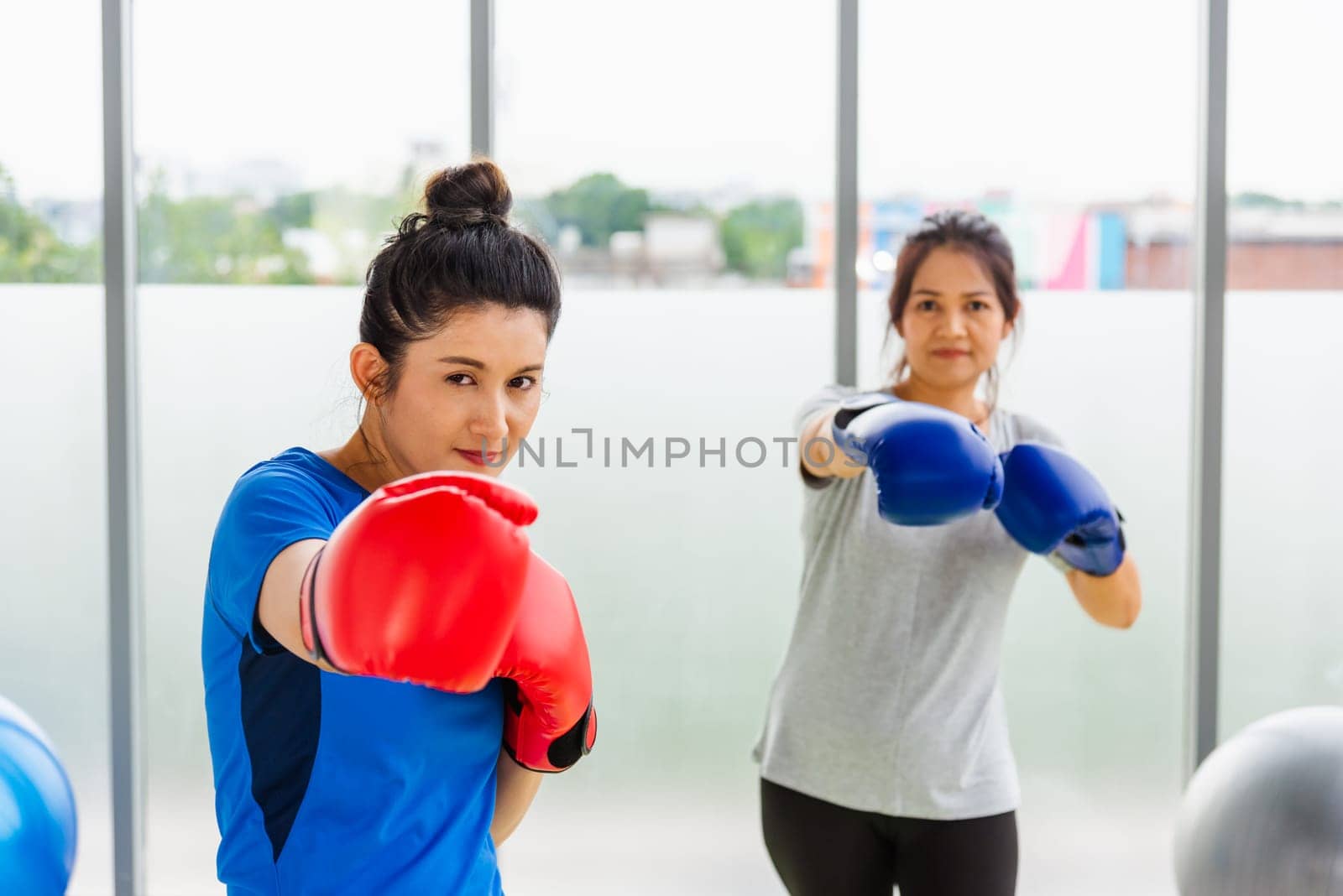 adult and young woman smiling sports fitness boxer wearing gloves practicing kick on boxing by Sorapop