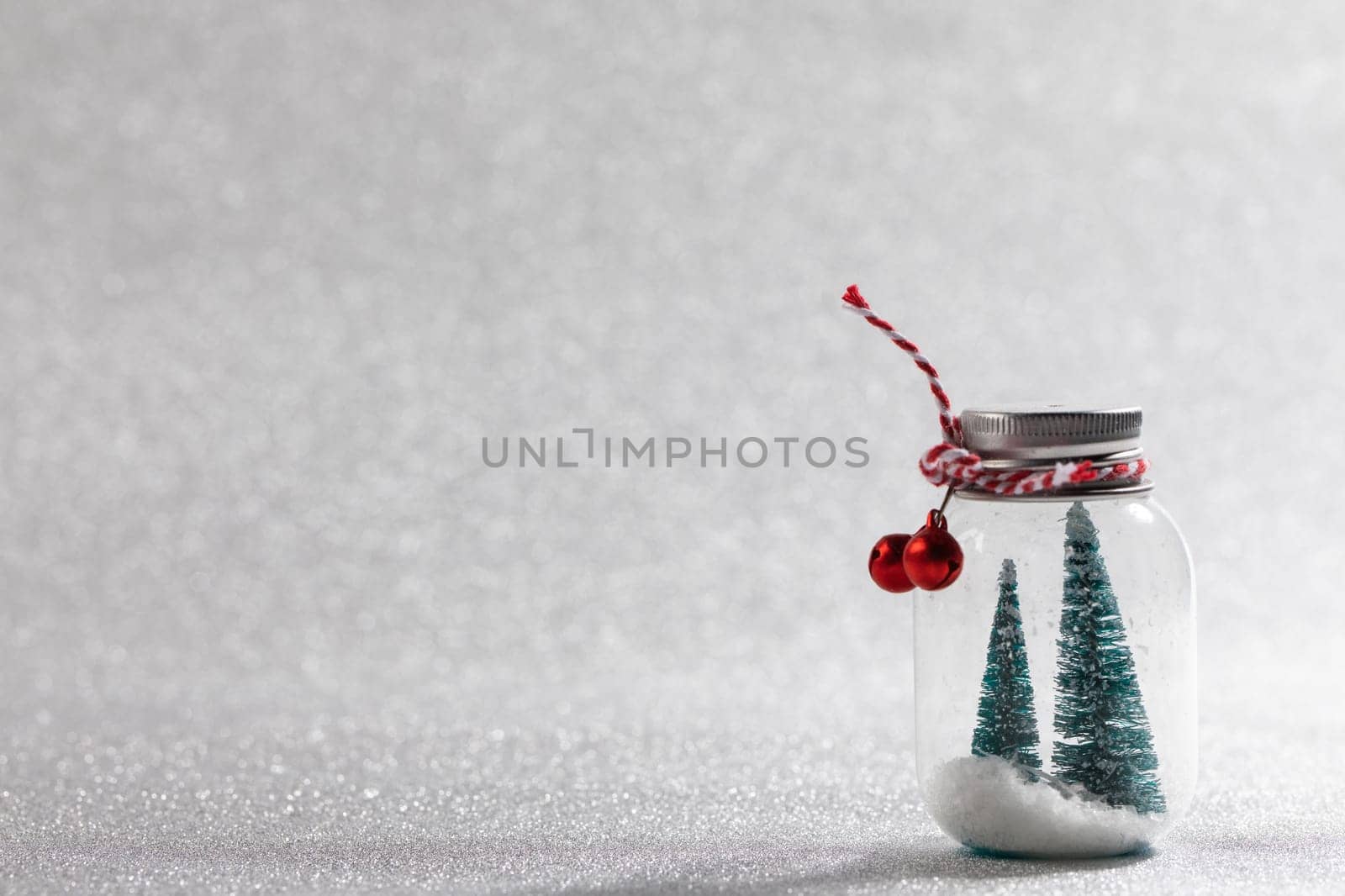 Christmas ornaments of glass jar with striped ribbon , bells and fir trees on snow inside on glitter background