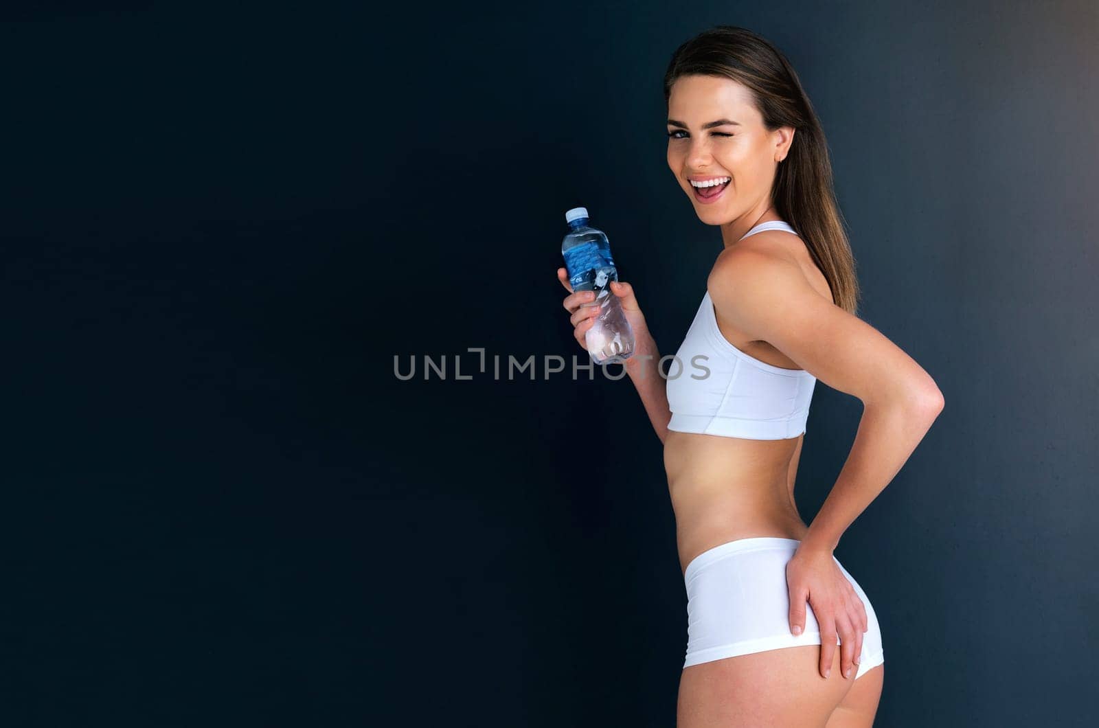 Happy woman, portrait and fitness with water bottle for lose weight, diet or natural nutrition against studio background. Attractive female person smile with drink for sustainability on mockup space by YuriArcurs