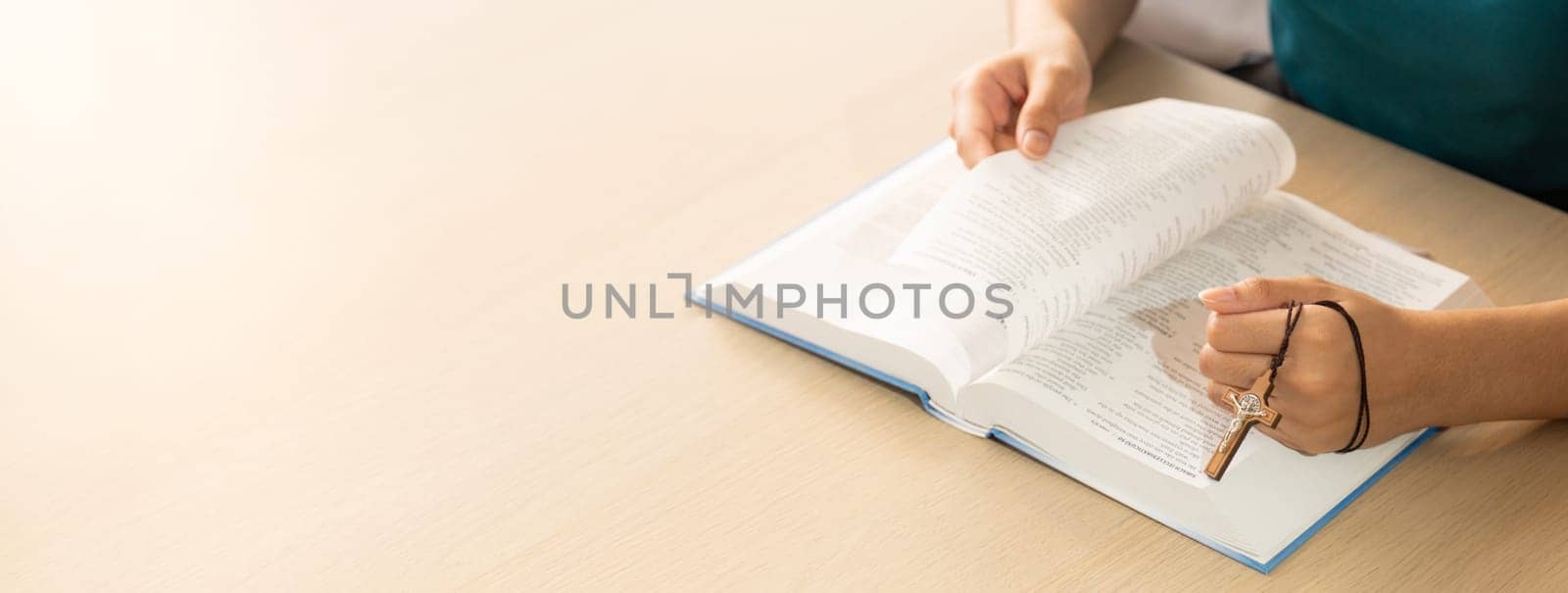 Cropped image of female reading a bible book while holding cross at wooden table with blurring background. Concept of hope, religion, faith, christianity and god blessing. Warm. Burgeoning.