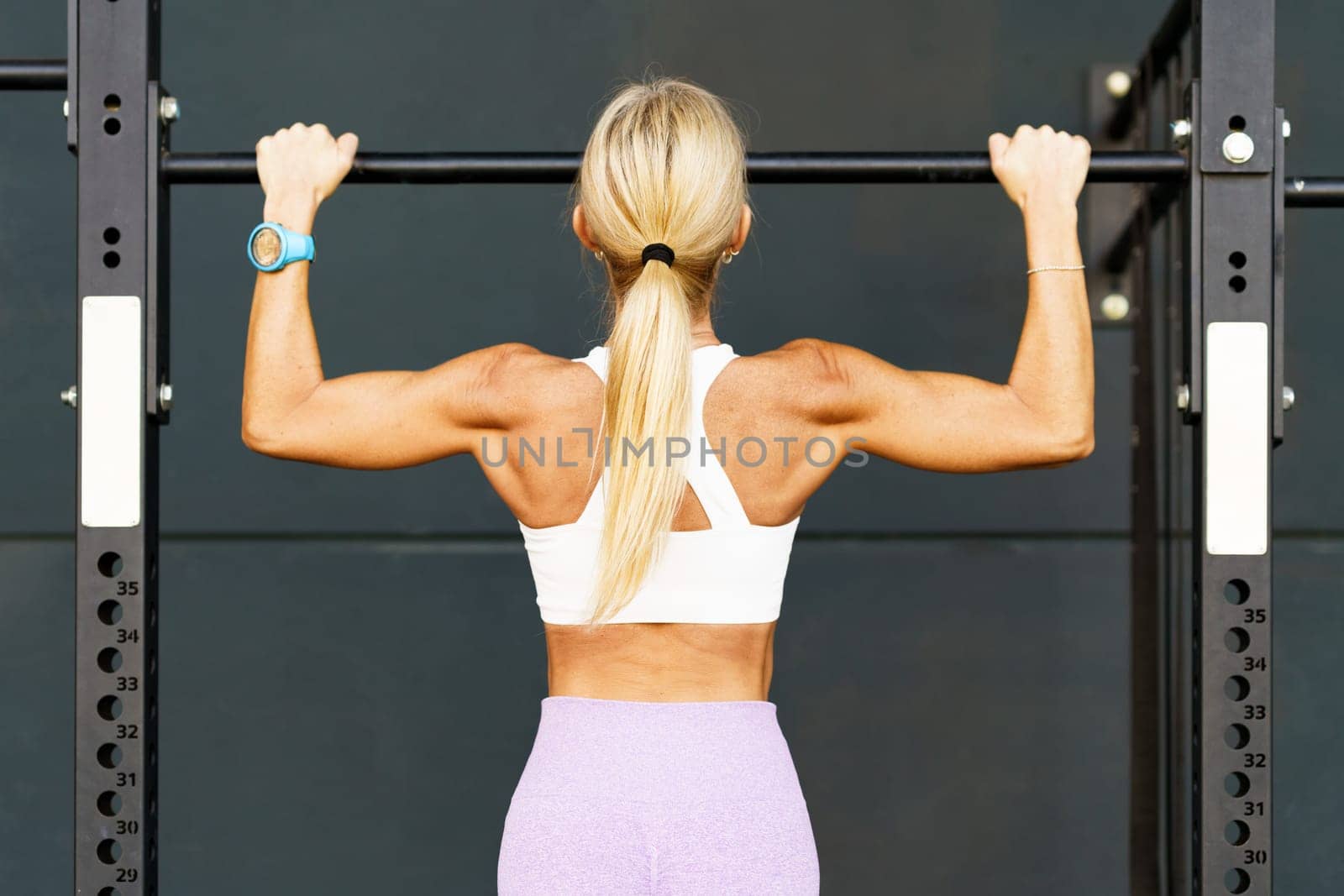 Back view of anonymous female athlete doing pulls up on horizontal bar during workout in gym