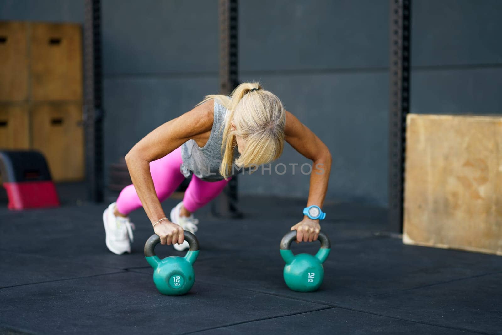 Unrecognizable sportswoman exercising push ups with kettlebell in gym by javiindy