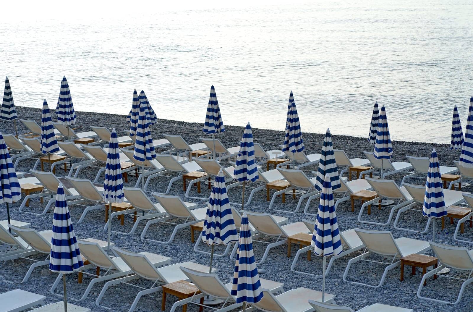 France, Nice. October 10, 2023. Striped blue and white umbrellas and sun loungers on the city beach. Umbrellas on the beach against the background of the sea by aprilphoto