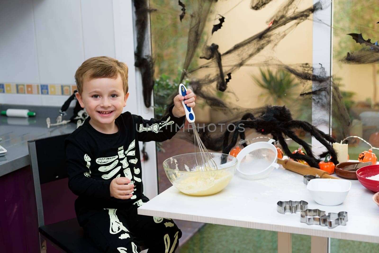boy dressed as a skeleton preparing halloween cookies.Happy boy preparing for halloween. Festival in the kitchen. by jcdiazhidalgo