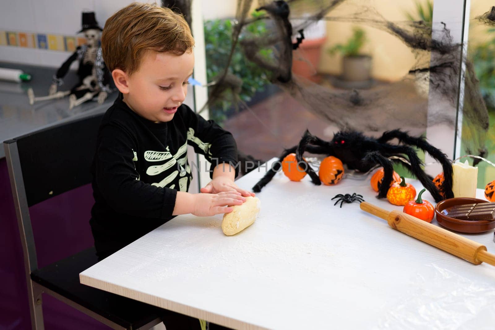boy dressed as a skeleton kneading flour to make halloween cookies at home. Preparing halloween by jcdiazhidalgo