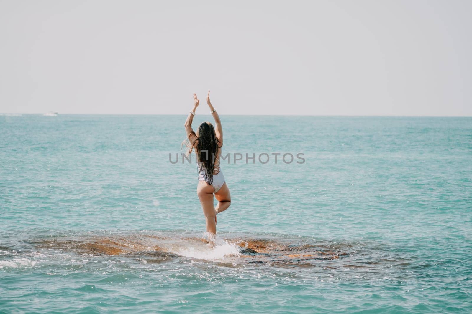 Woman sea yoga. Back view of free calm happy satisfied woman with long hair standing on top rock with yoga position against of sky by the sea. Healthy lifestyle outdoors in nature, fitness concept.