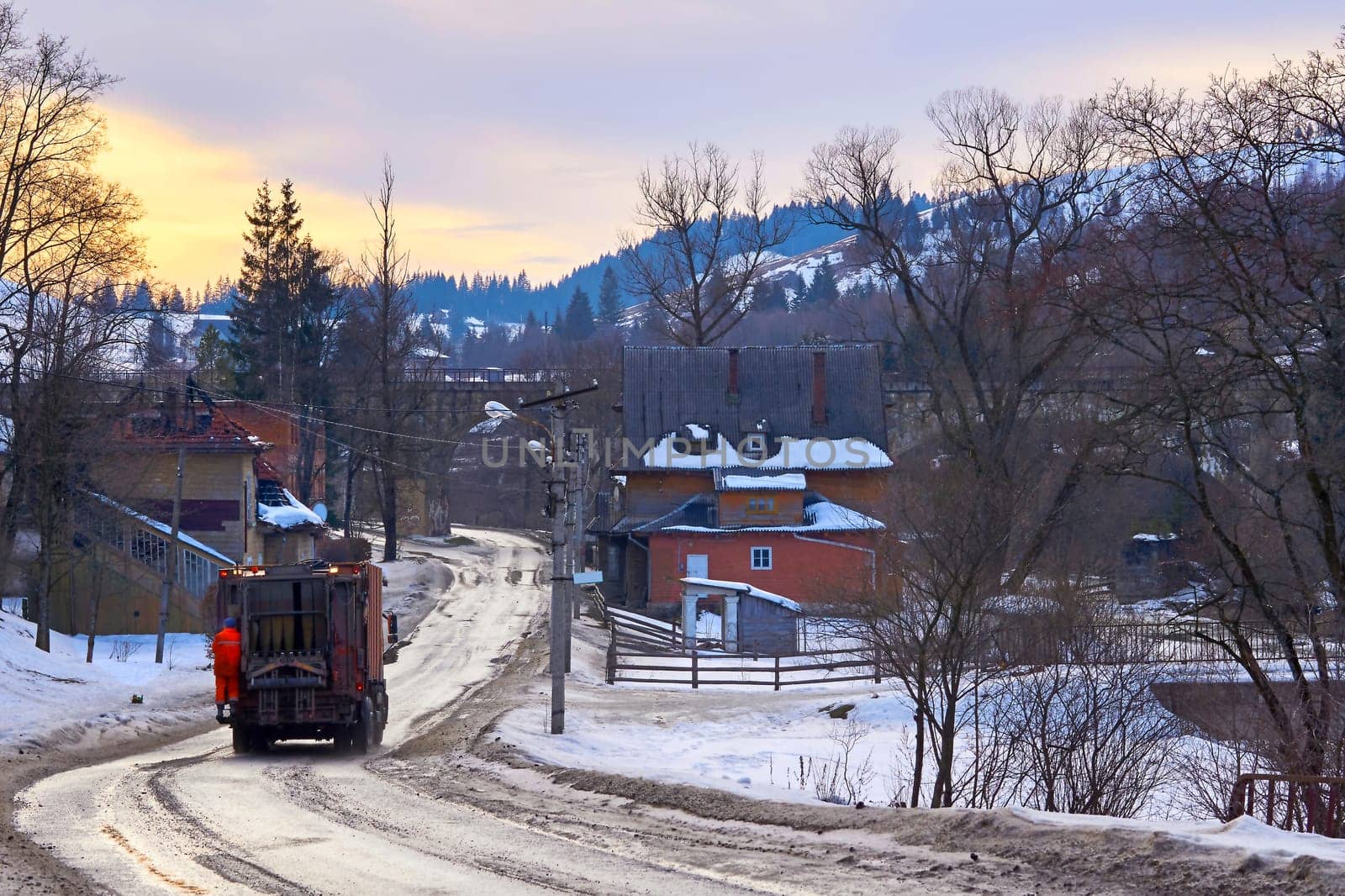 A truck collecting garbage drives through an evening winter town by jovani68