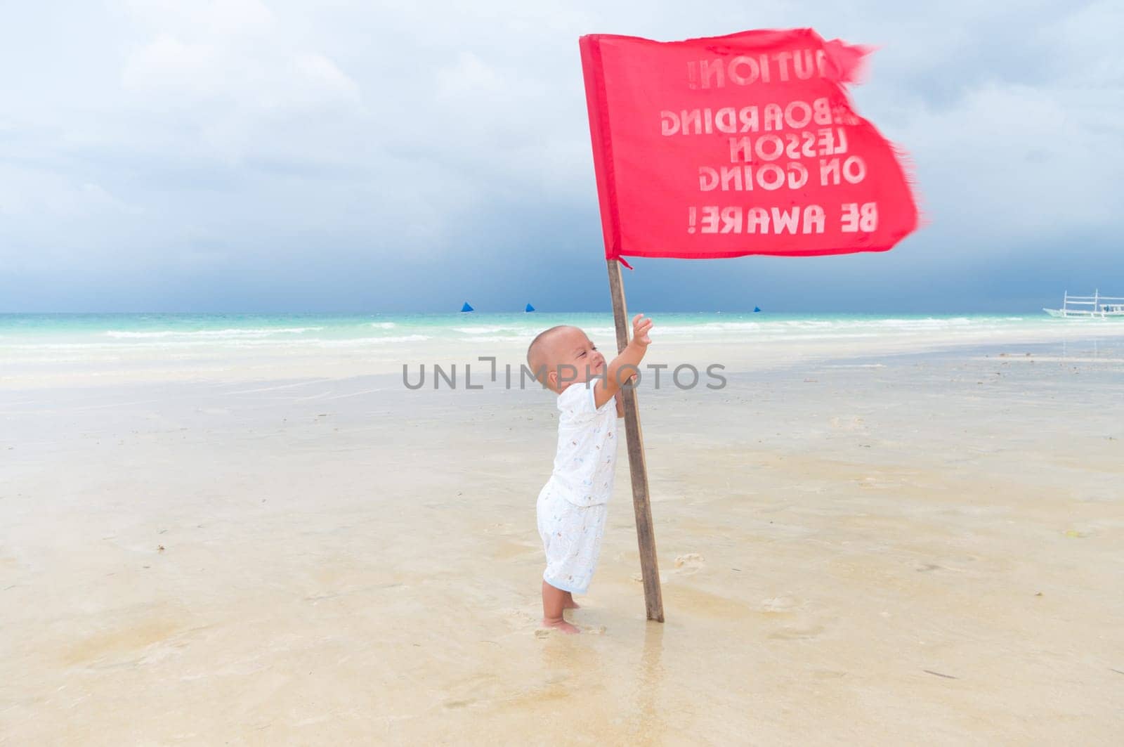 baby trying to grab a red flag on a tropical beach