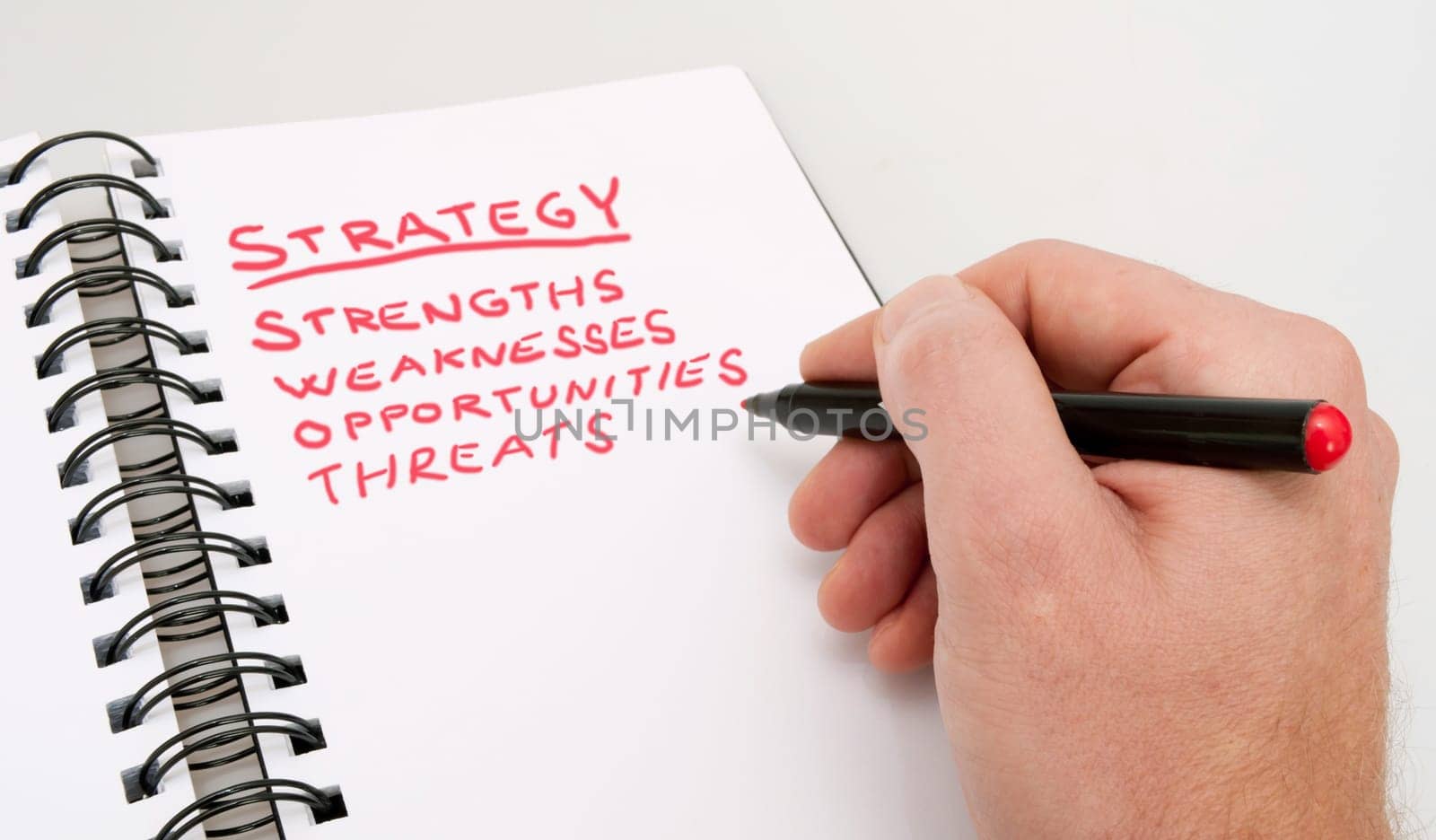 SWOT Analysis - Close up of Hand With Red Marker and Open Notebook