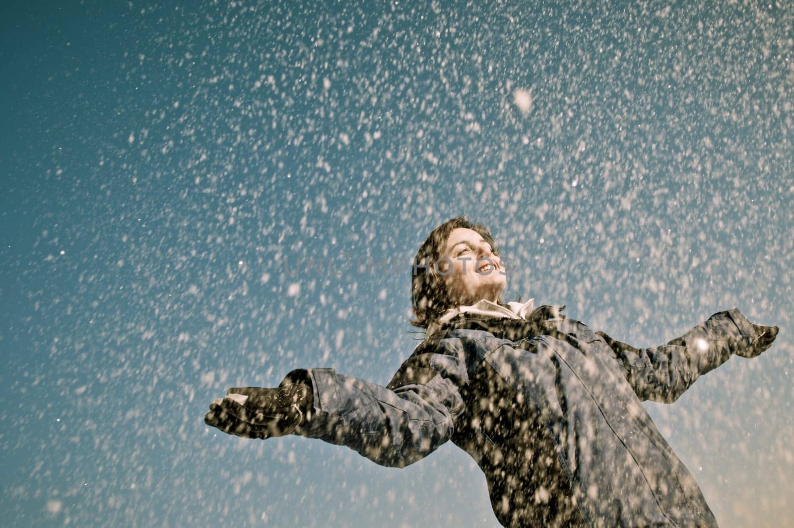 Young woman throwing snow on blue sky in background - joy and happines emotions