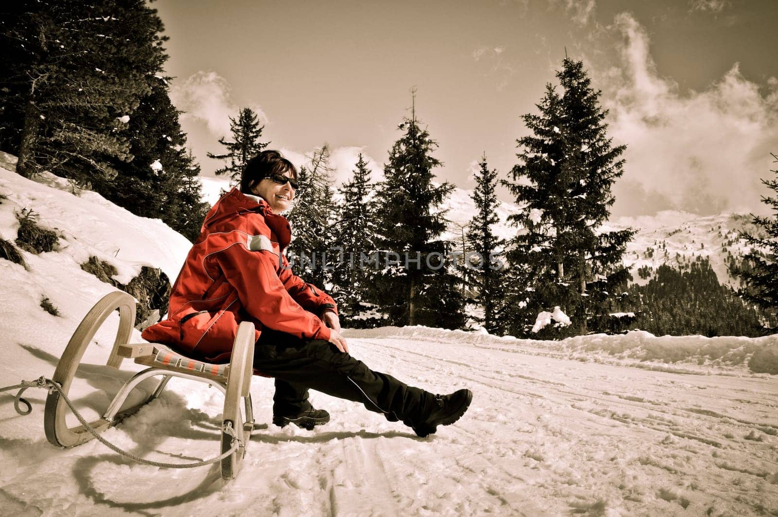 Senior woman siting on sledge sunning in mountain winter snow country with blue sky
