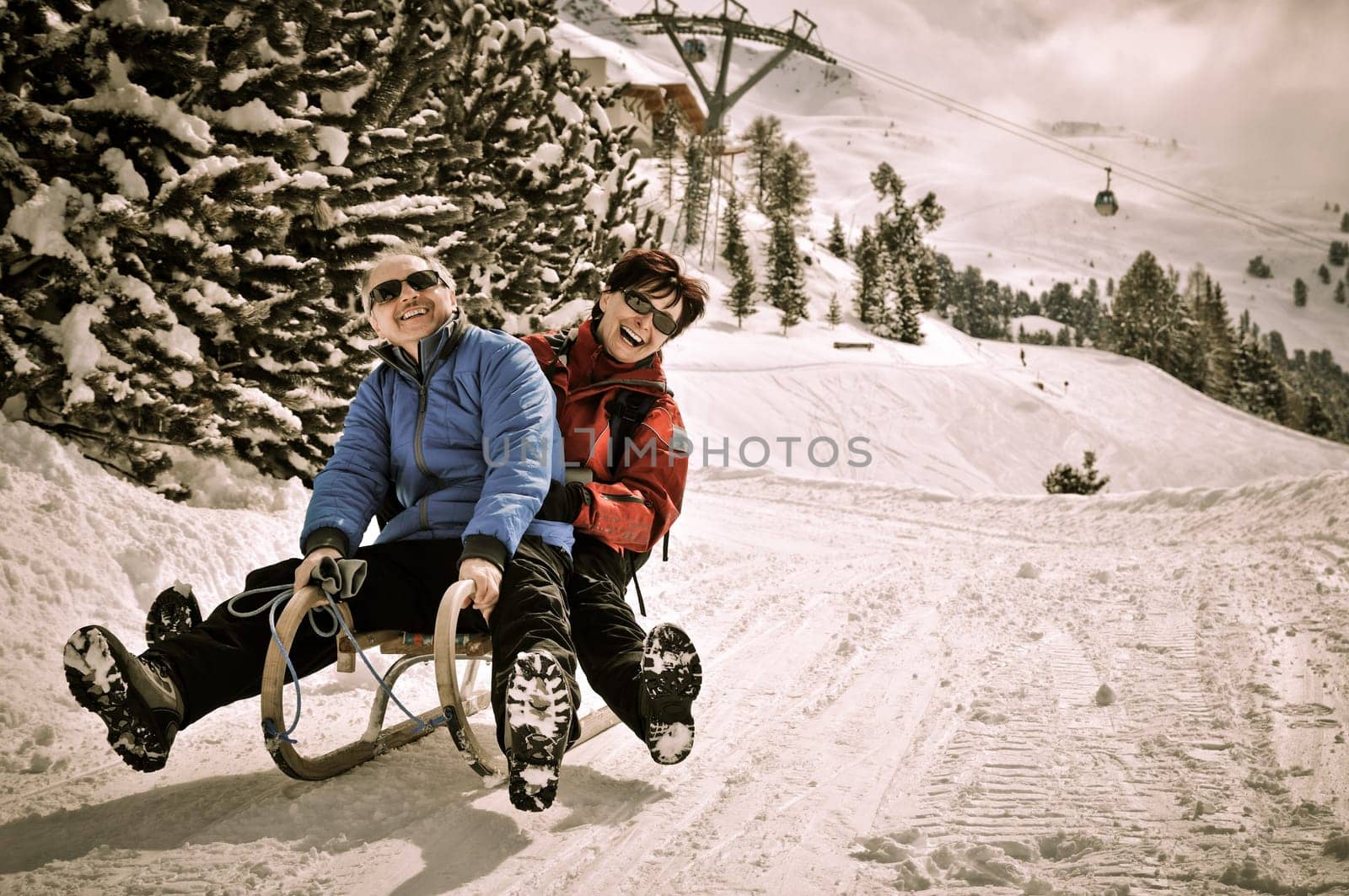 Active senior couple on sledge having fun in mountain snowy country