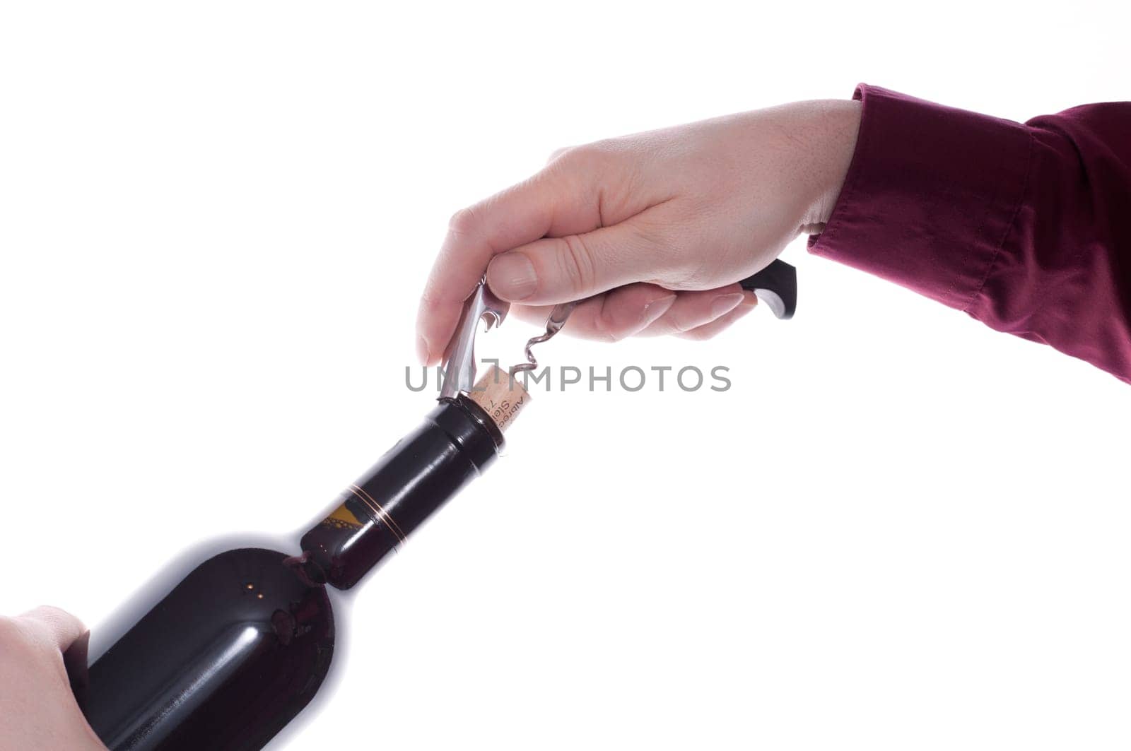 A corkscrew pulls a cork out of a wine bottle with red wine