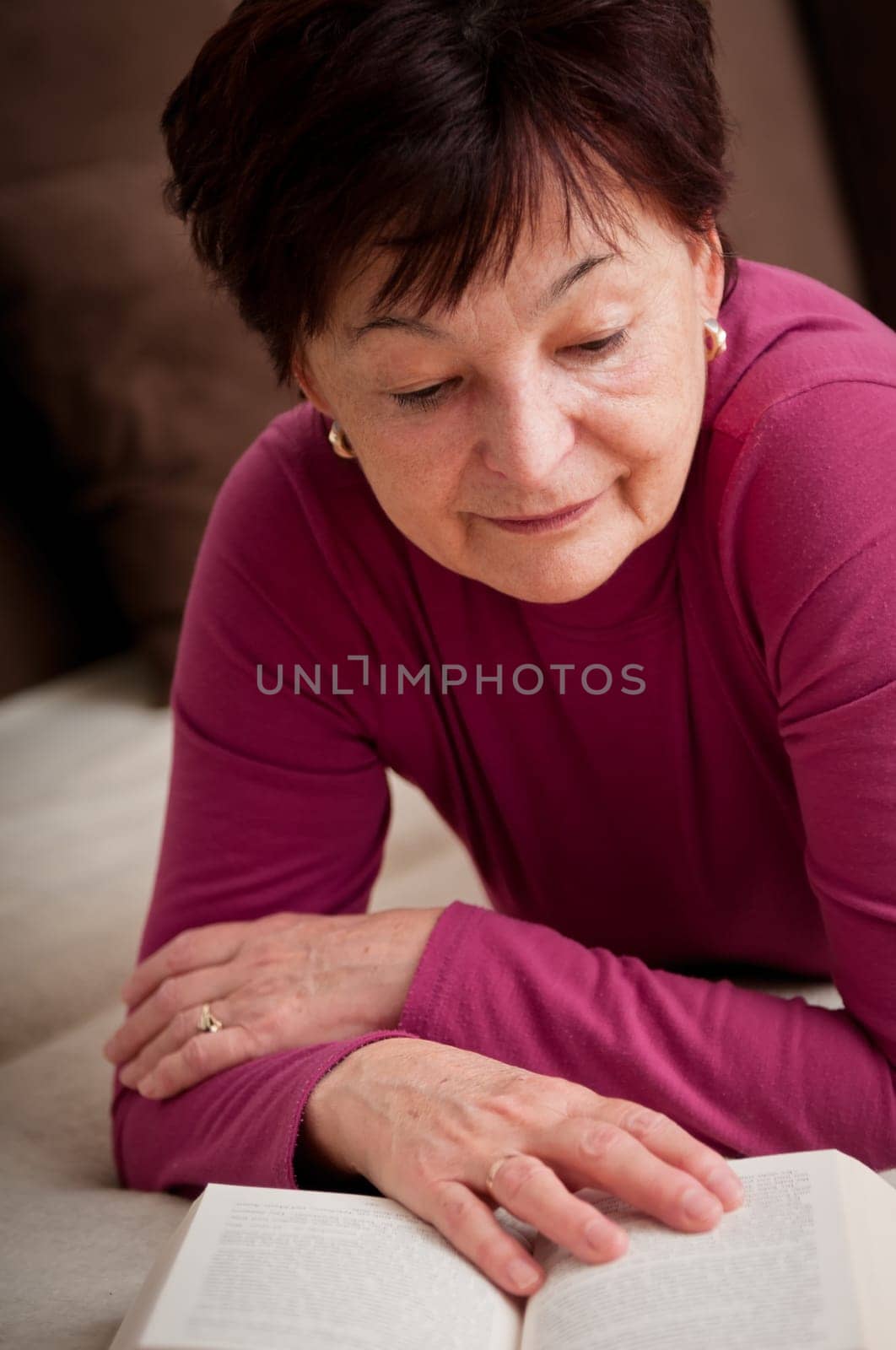 Senior woman reading book at home on sofa
