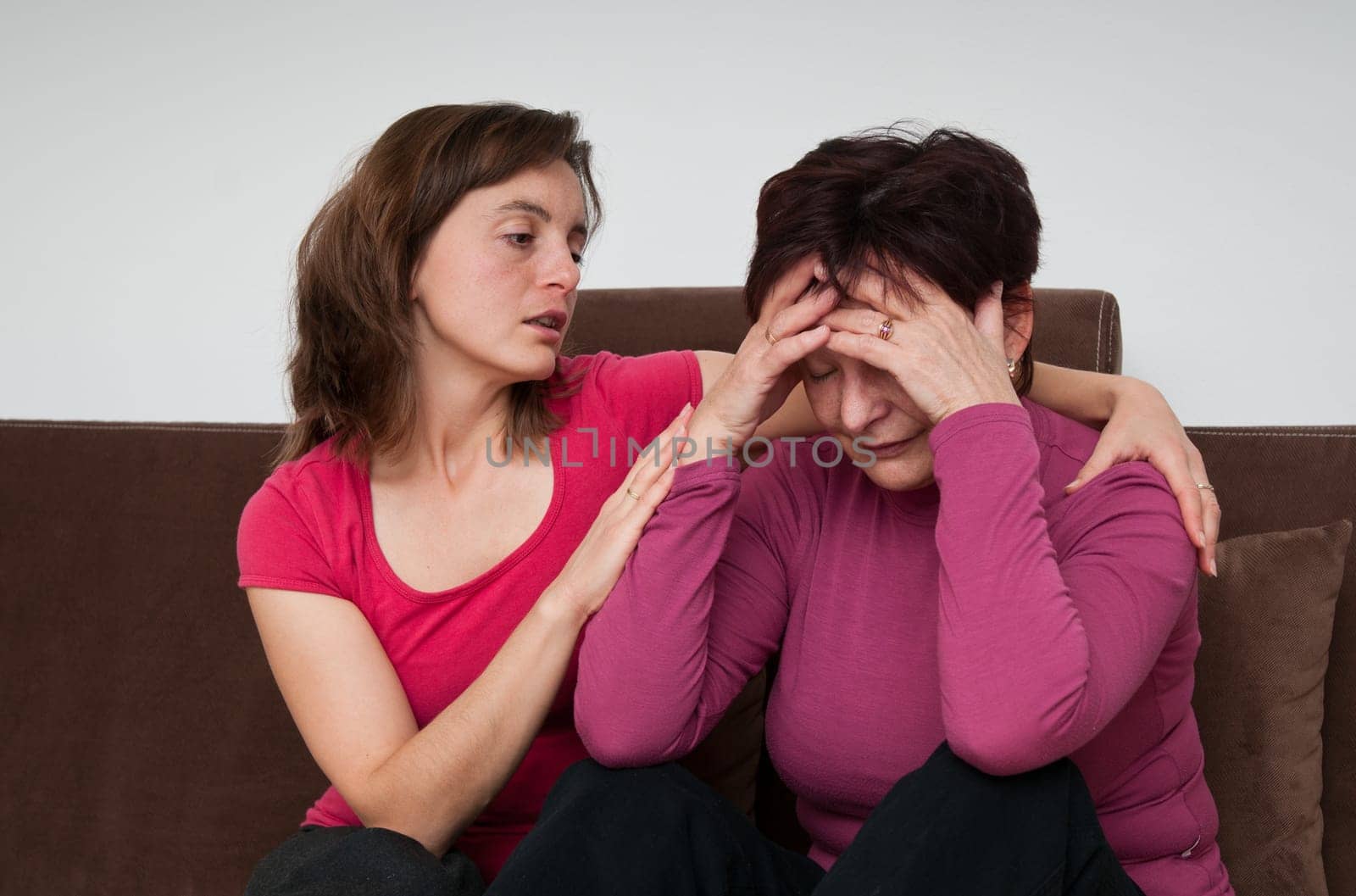 Daughter (young woman) comforts her depressed senior mother at home