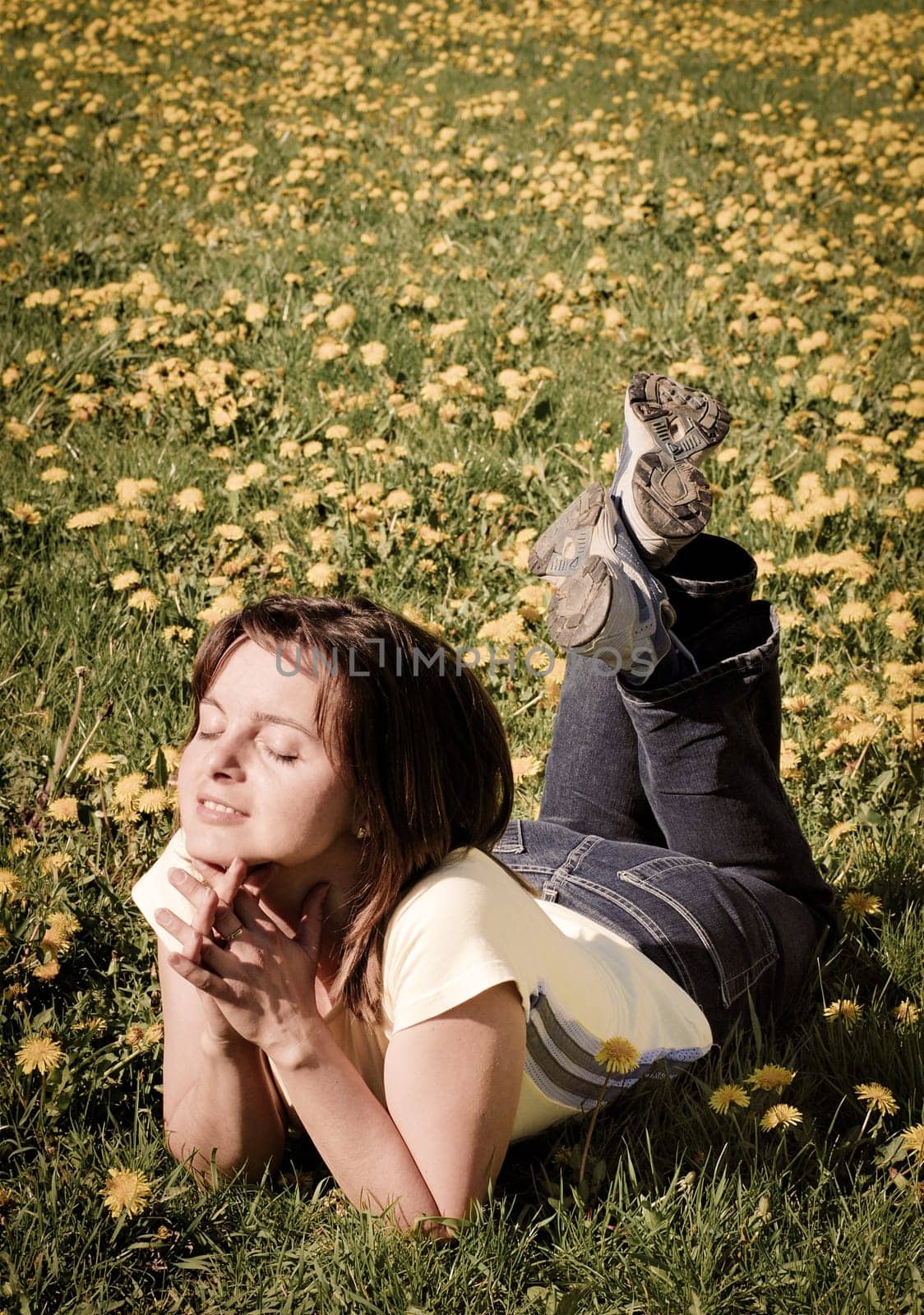 Woman lying in field of dandelions with face turned to sun