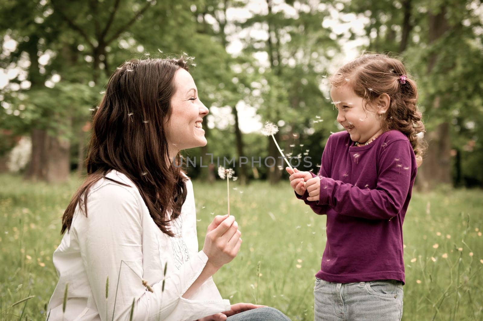 Mother with small daughter blowing to dandelion - lifestyle outdoors scene in park