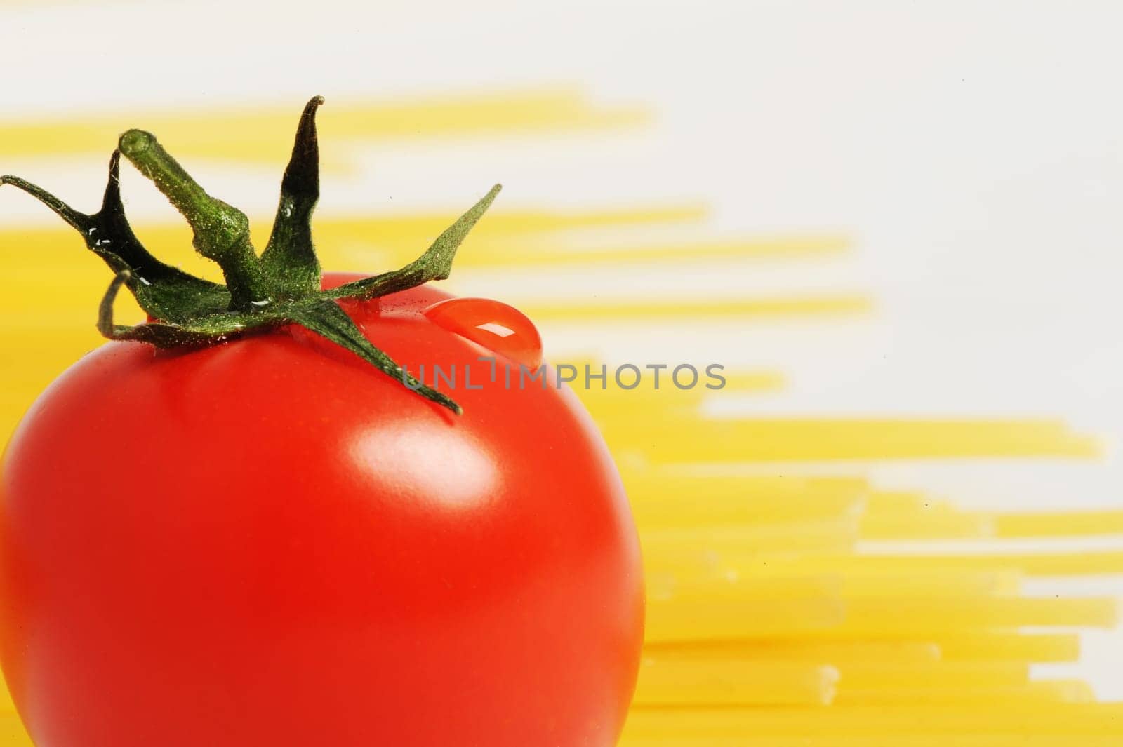 Tomato with drops and uncooked spaghetti noodleson background